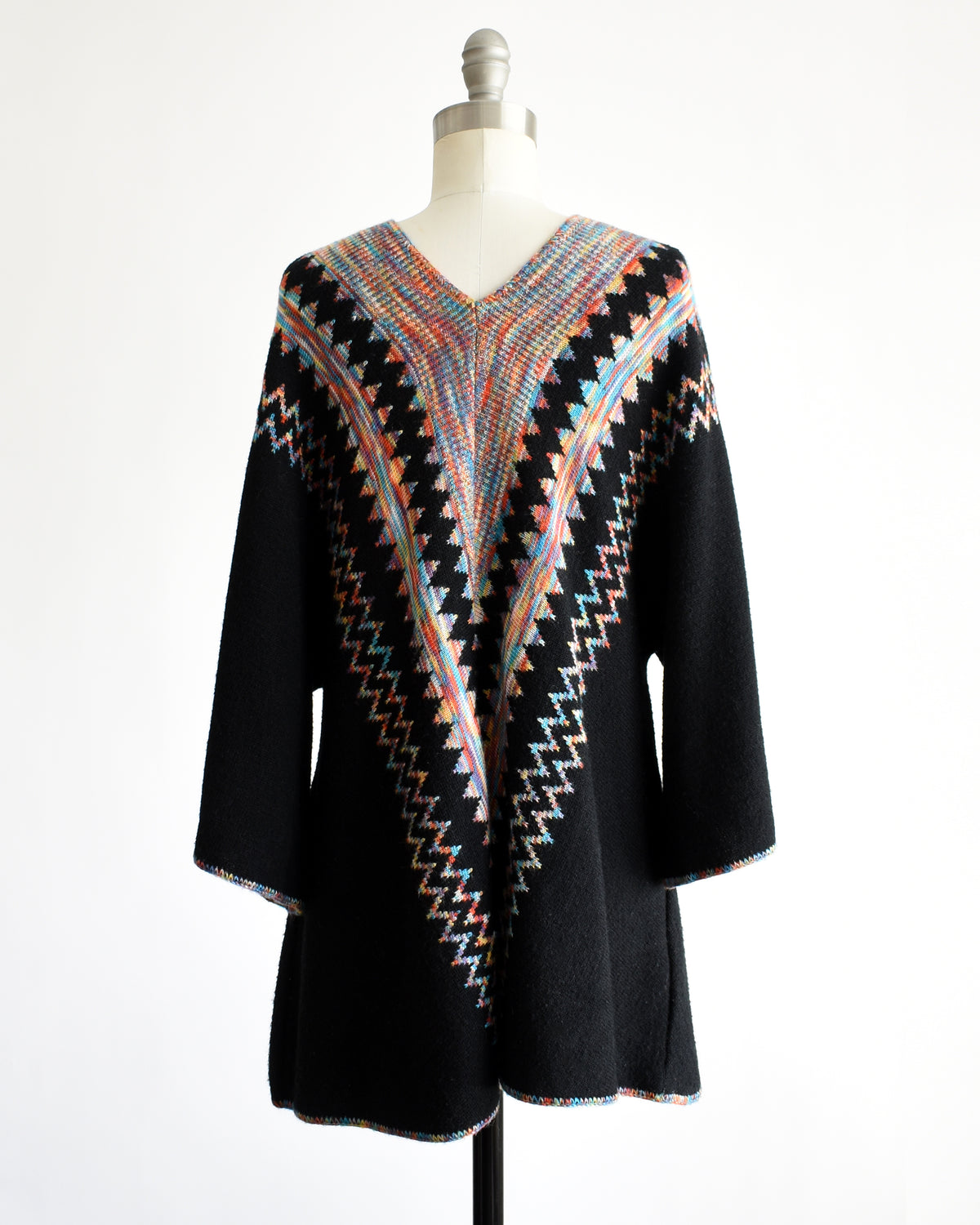 back view of a vintage 1970s  black three-quarter sleeve tunic top with a colorful geometric zigzag pattern down the front, displayed on a mannequin against a white background.