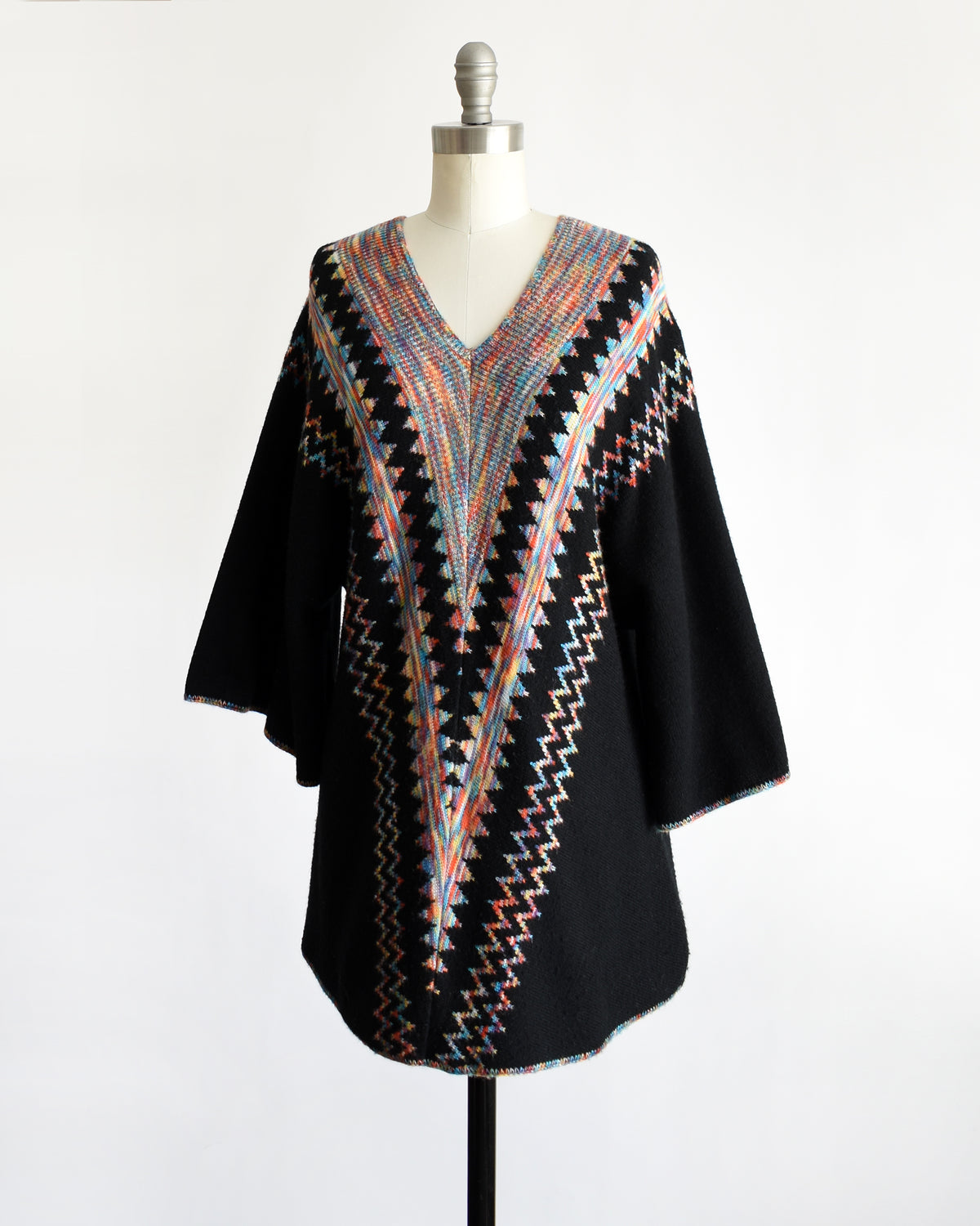 side front view of a vintage 1970s  black three-quarter sleeve tunic top with a colorful geometric zigzag pattern down the front, displayed on a mannequin against a white background.
