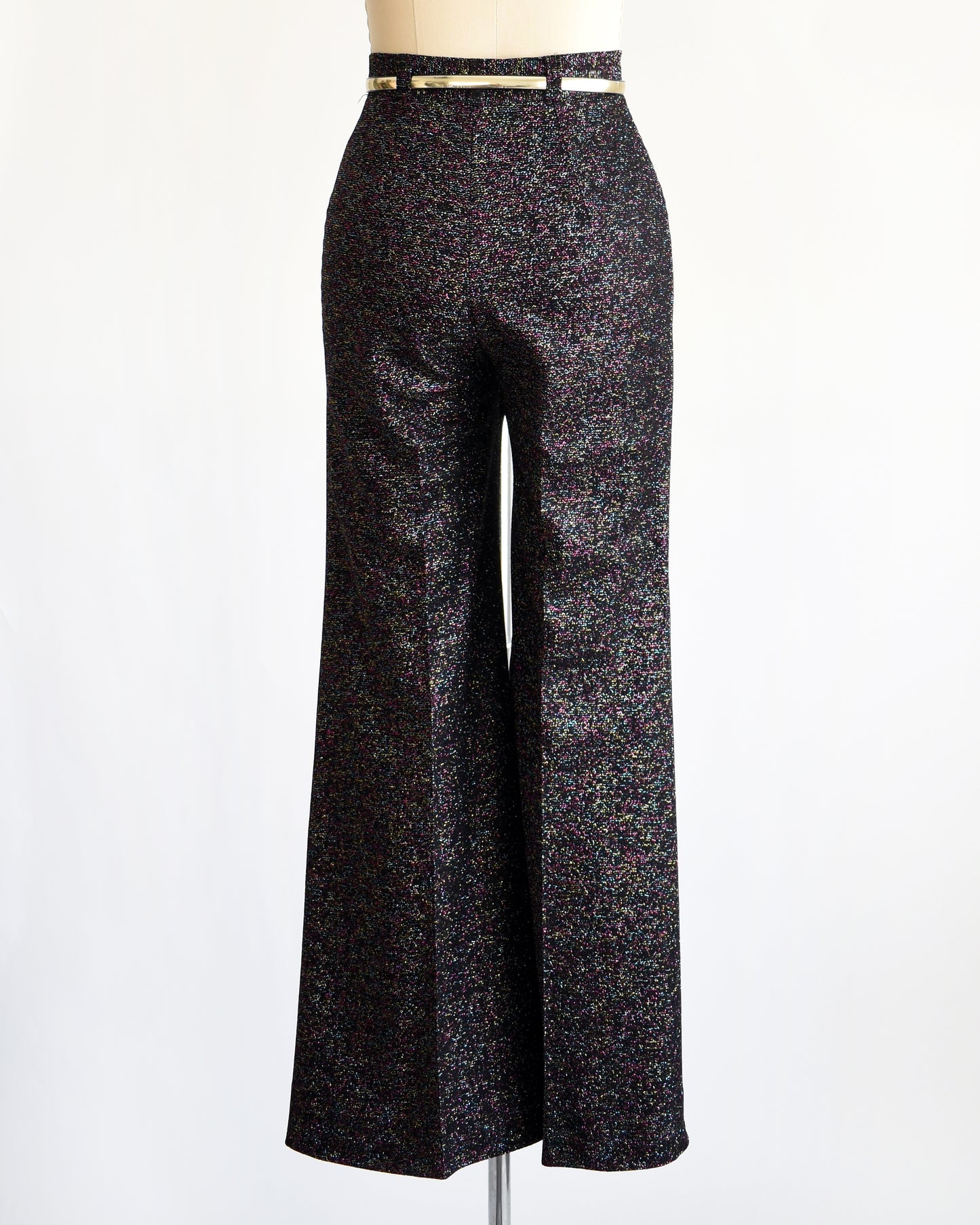 back view of a pair of vintage 1970s black rainbow metallic pants with a silver belt on a mannequin against a white background