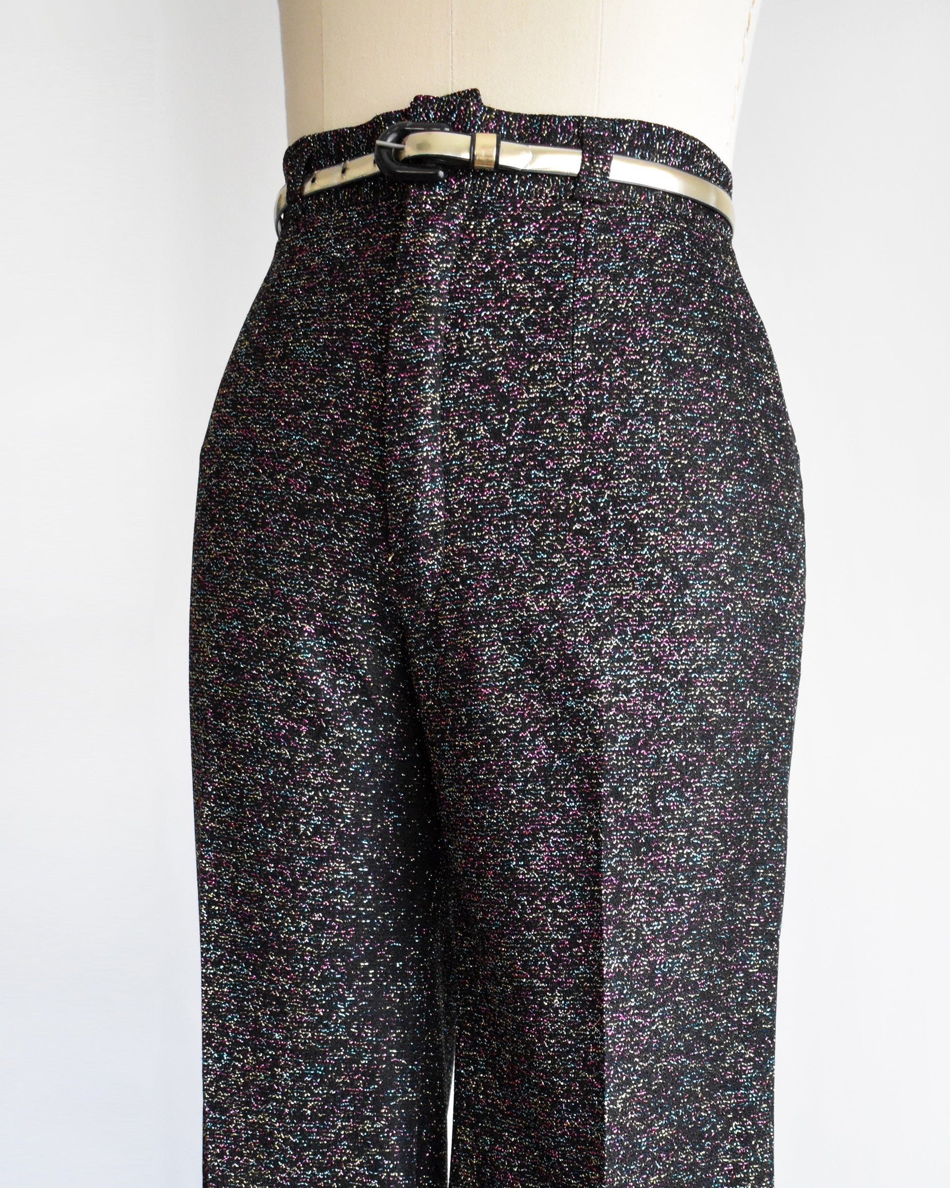 side front view of a pair of vintage 1970s black rainbow metallic pants with a silver belt on a mannequin against a white background