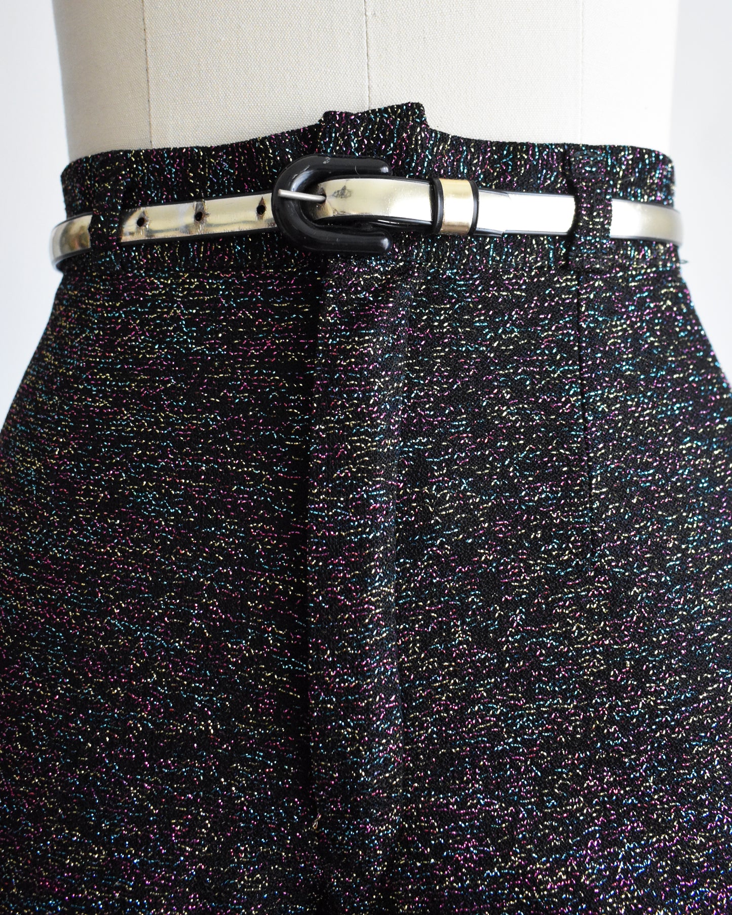 close up of the waist and belt of a pair of vintage 1970s black rainbow metallic pants with a silver belt on a mannequin against a white background