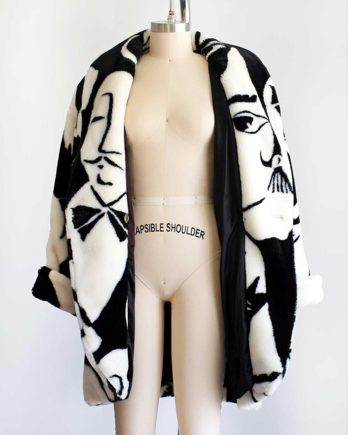 a vintage 1980s Donnybrook black and white graphic face patterned plush coat displayed on a mannequin against a plain white background. the coat is open showing the black lining