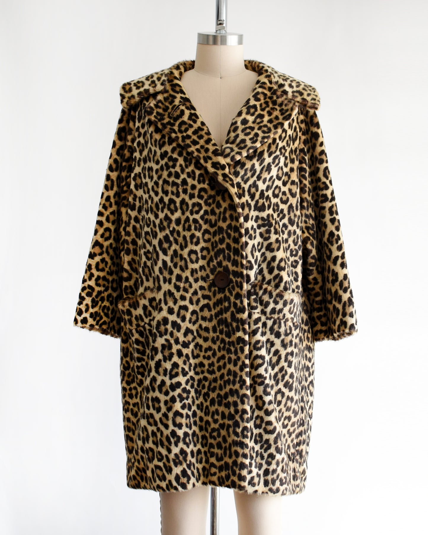 a vintage 1960s faux fur leopard print coat on a dress form against a white background. The top button is unbuttoned in this photo.