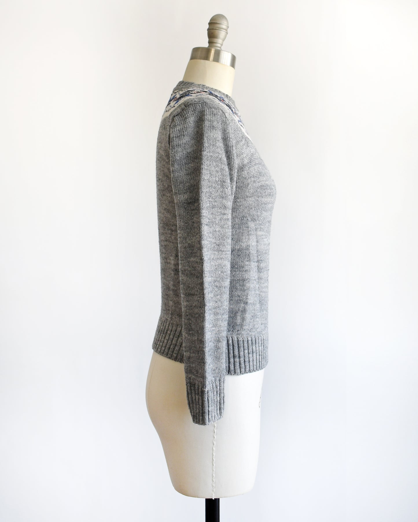 side view of a vintage 70s gray sweater with snowflake patterned neckline on a mannequin against a white background