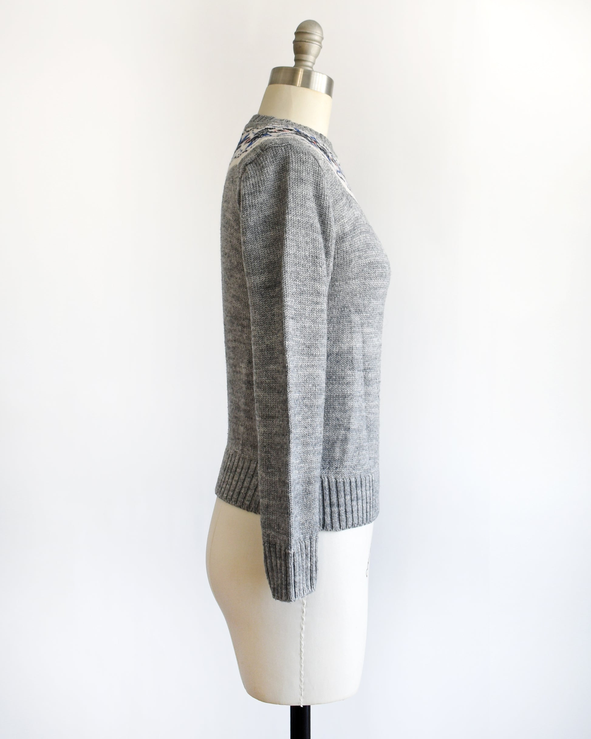 side view of a vintage 70s gray sweater with snowflake patterned neckline on a mannequin against a white background