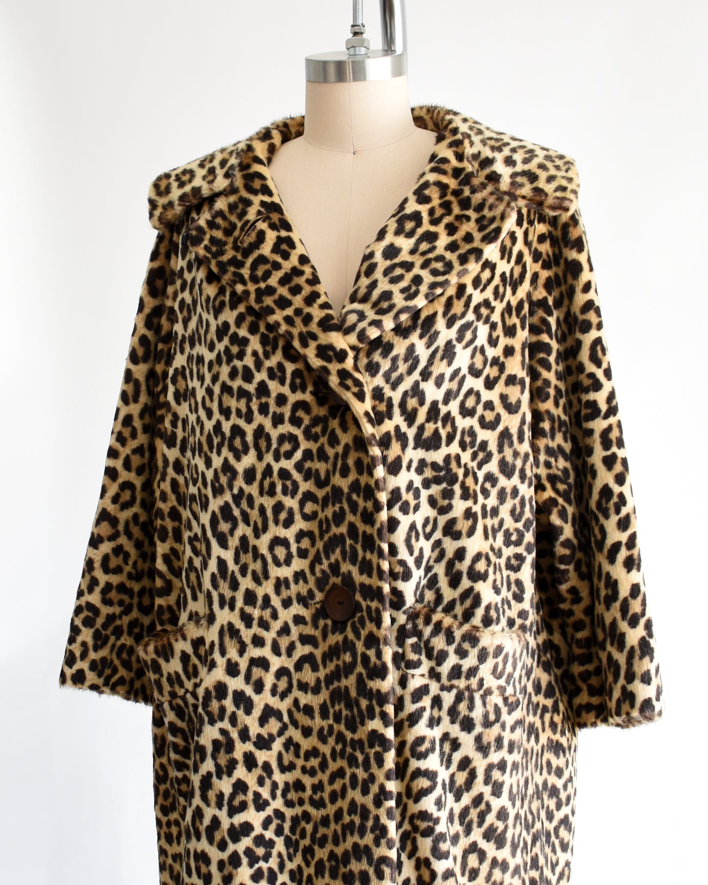side front view of a vintage 1960s faux fur leopard print coat on a dress form against a white background. The top button is unbuttoned in this photo.