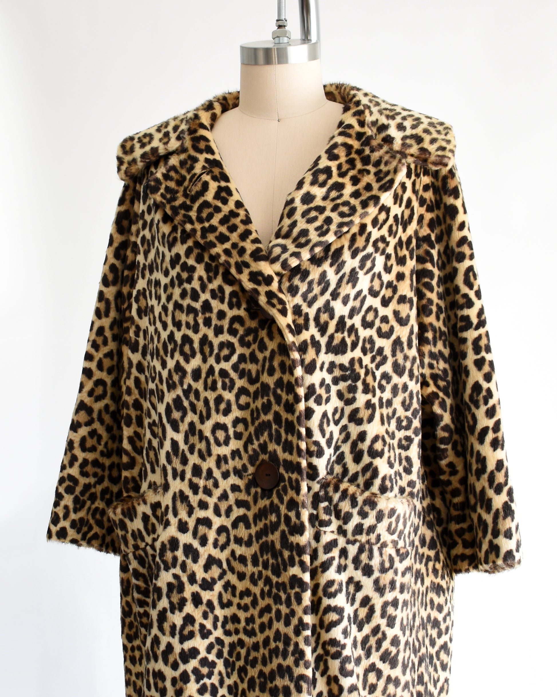 side front view of a vintage 1960s faux fur leopard print coat on a dress form against a white background. The top button is unbuttoned in this photo.