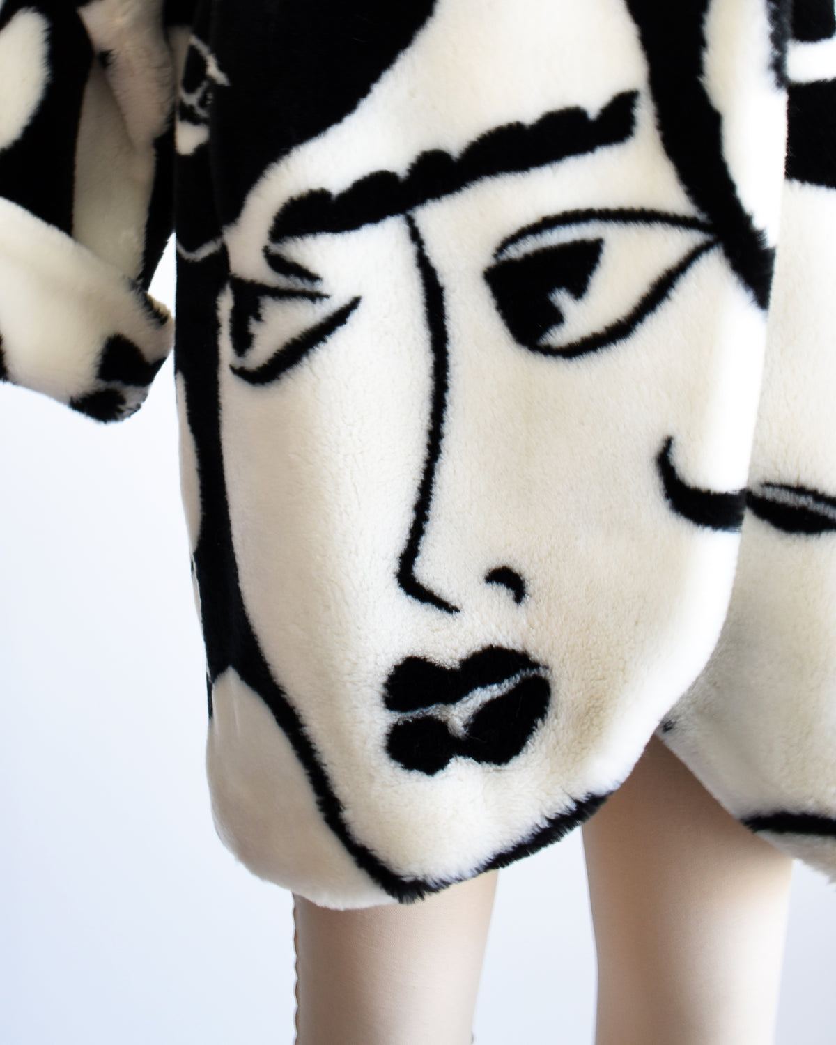 close up of a face on a vintage 1980s Donnybrook black and white graphic face patterned plush coat displayed on a mannequin against a plain white background.