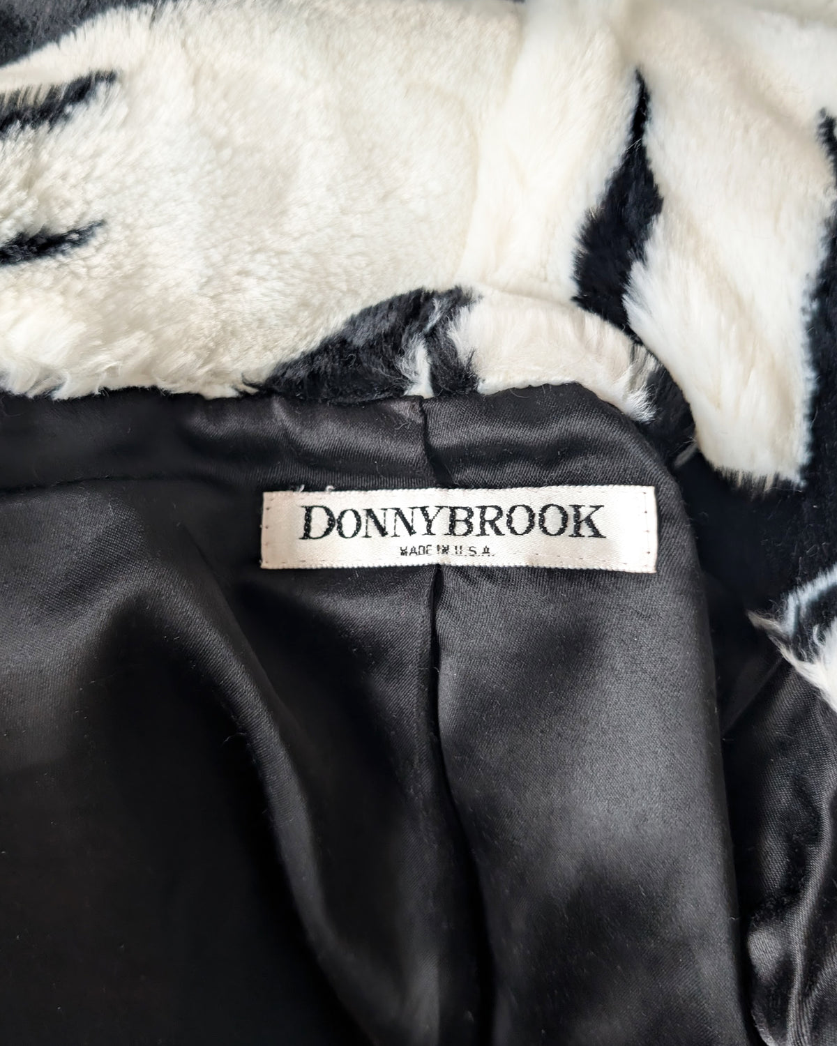 Close-up of a black satin-lined coat with a white faux-fur collar and a visible DONNYBROOK brand label.