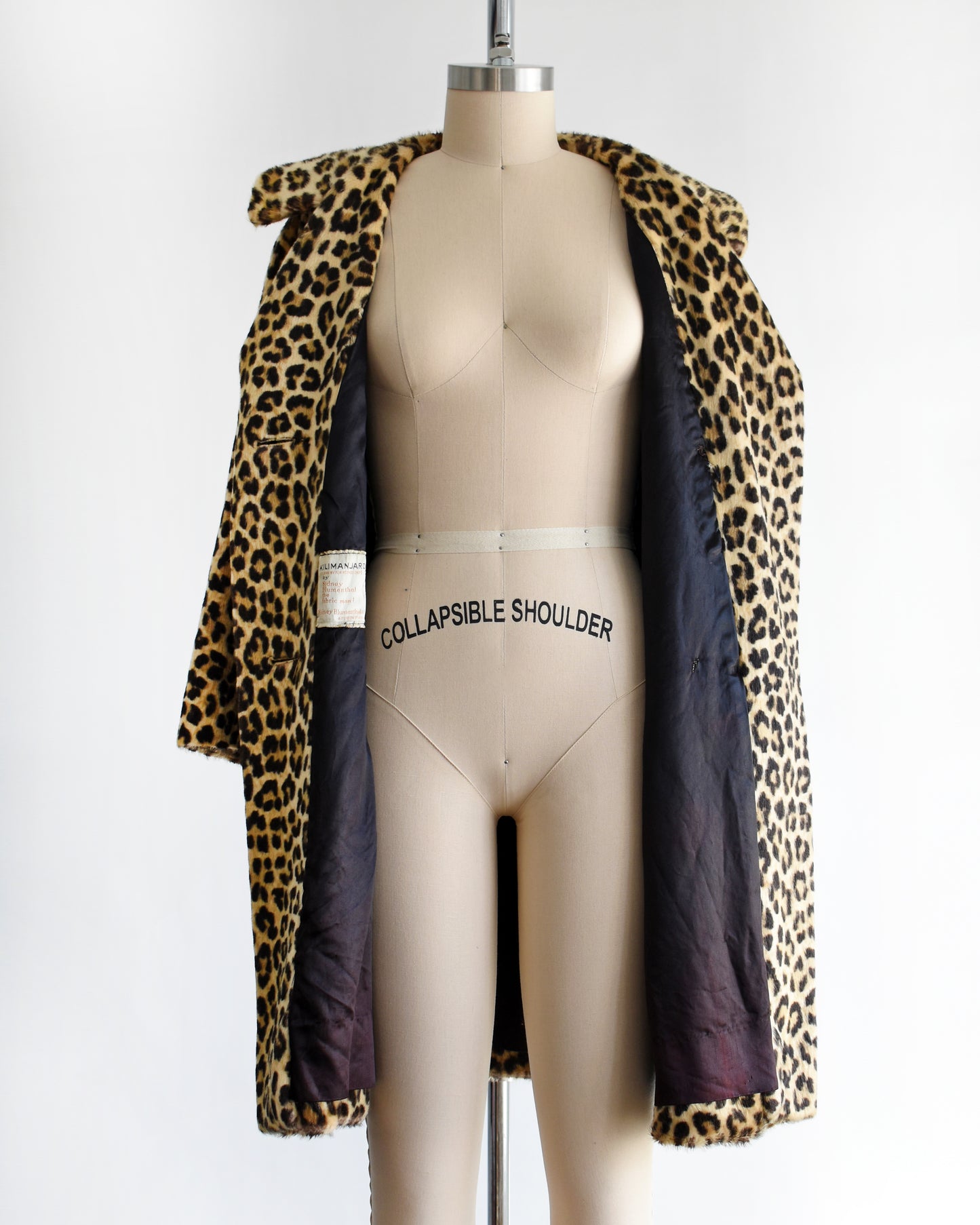 a vintage 1960s faux fur leopard print coat on a dress form against a white background. The coat is open in this photo