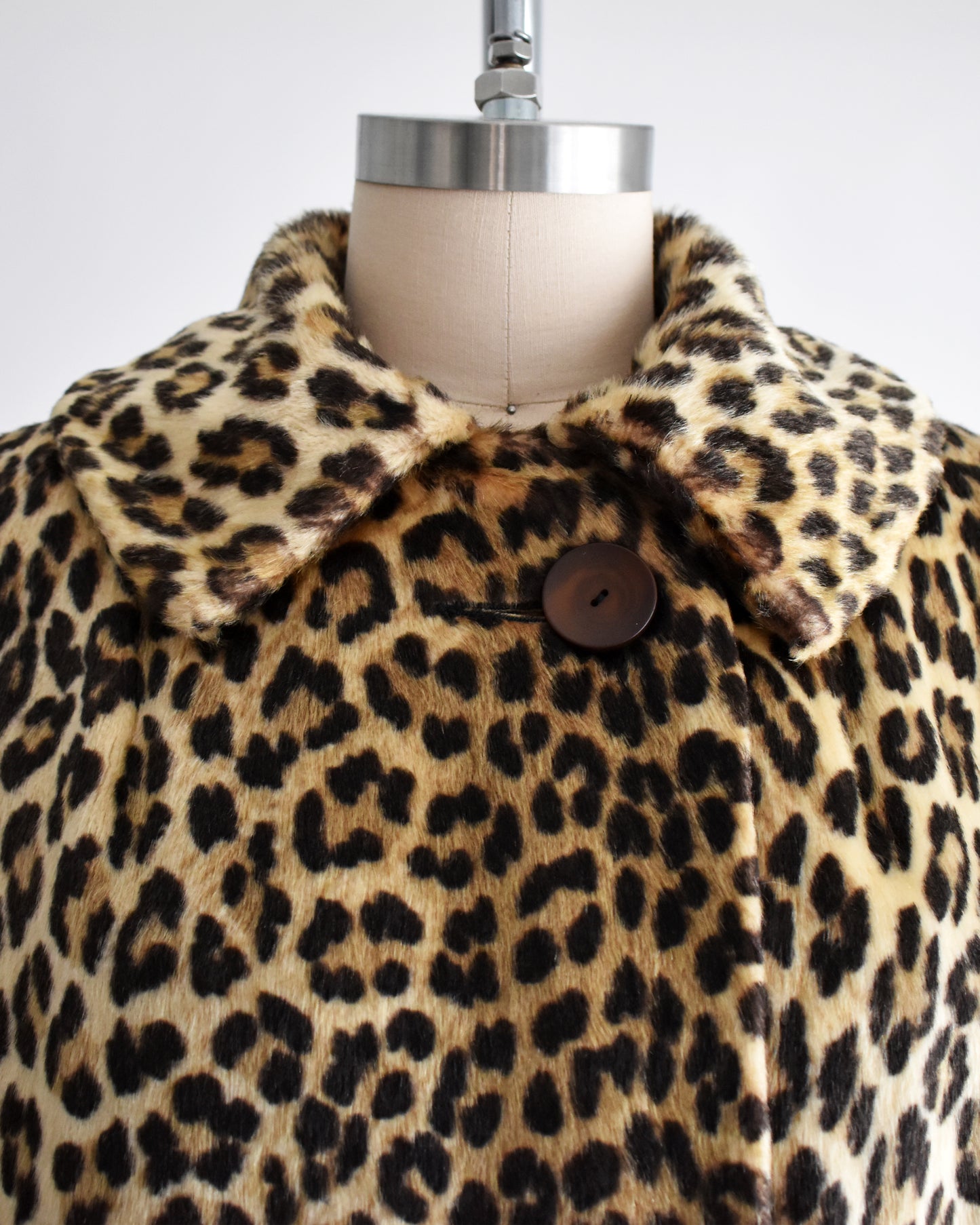 close up of the collar and top button of a vintage 1960s faux fur leopard print coat on a dress form against a white background