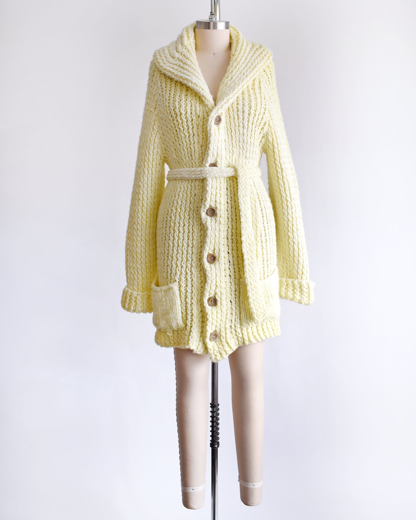 A vintage 1970s cream chunky knit cardigan with wood buttons down the front with a matching tie belt on a dress form.