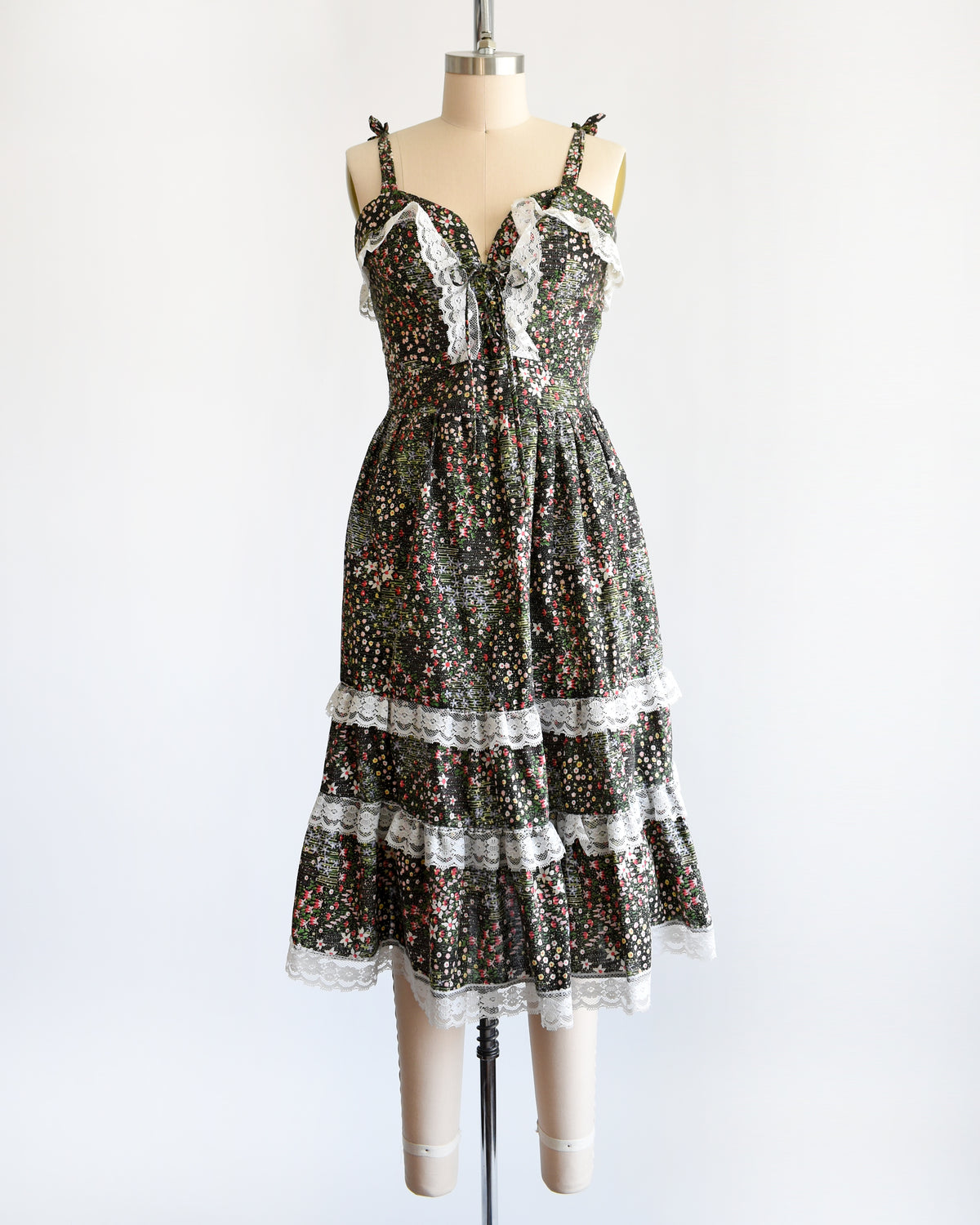 a vintage 1970s dark floral and lace trim dress on a cream dress form against a white background
