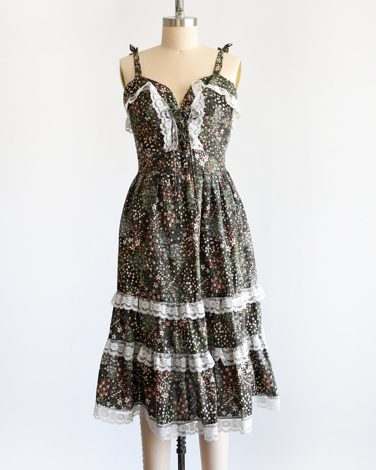 a vintage 1970s dark floral and lace trim dress on a cream dress form against a white background