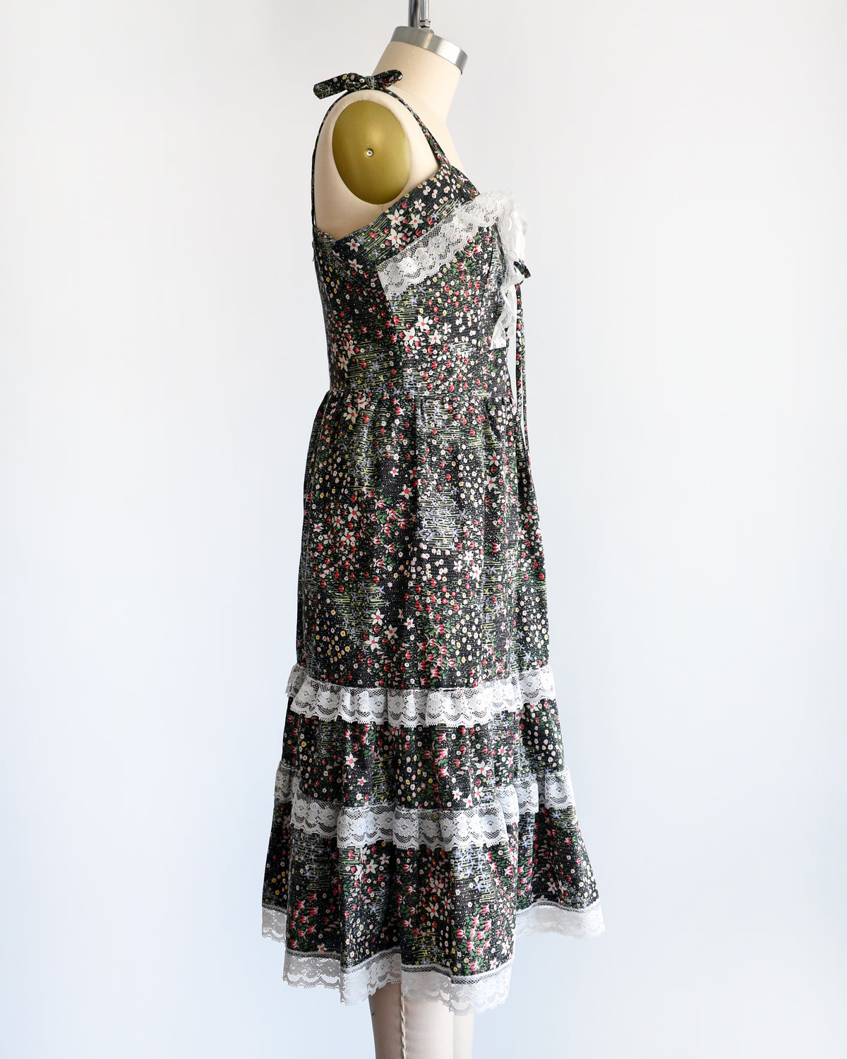 side view of a vintage 1970s dark floral and lace trim dress on a cream dress form against a white background