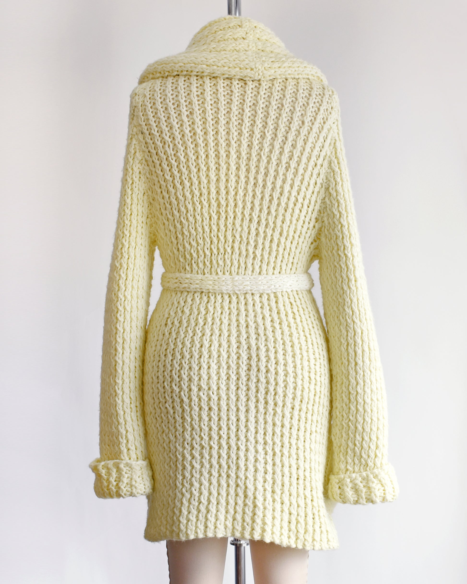 back view of a vintage 1970s cream chunky knit cardigan with wood buttons down the front with a matching tie belt on a dress form.