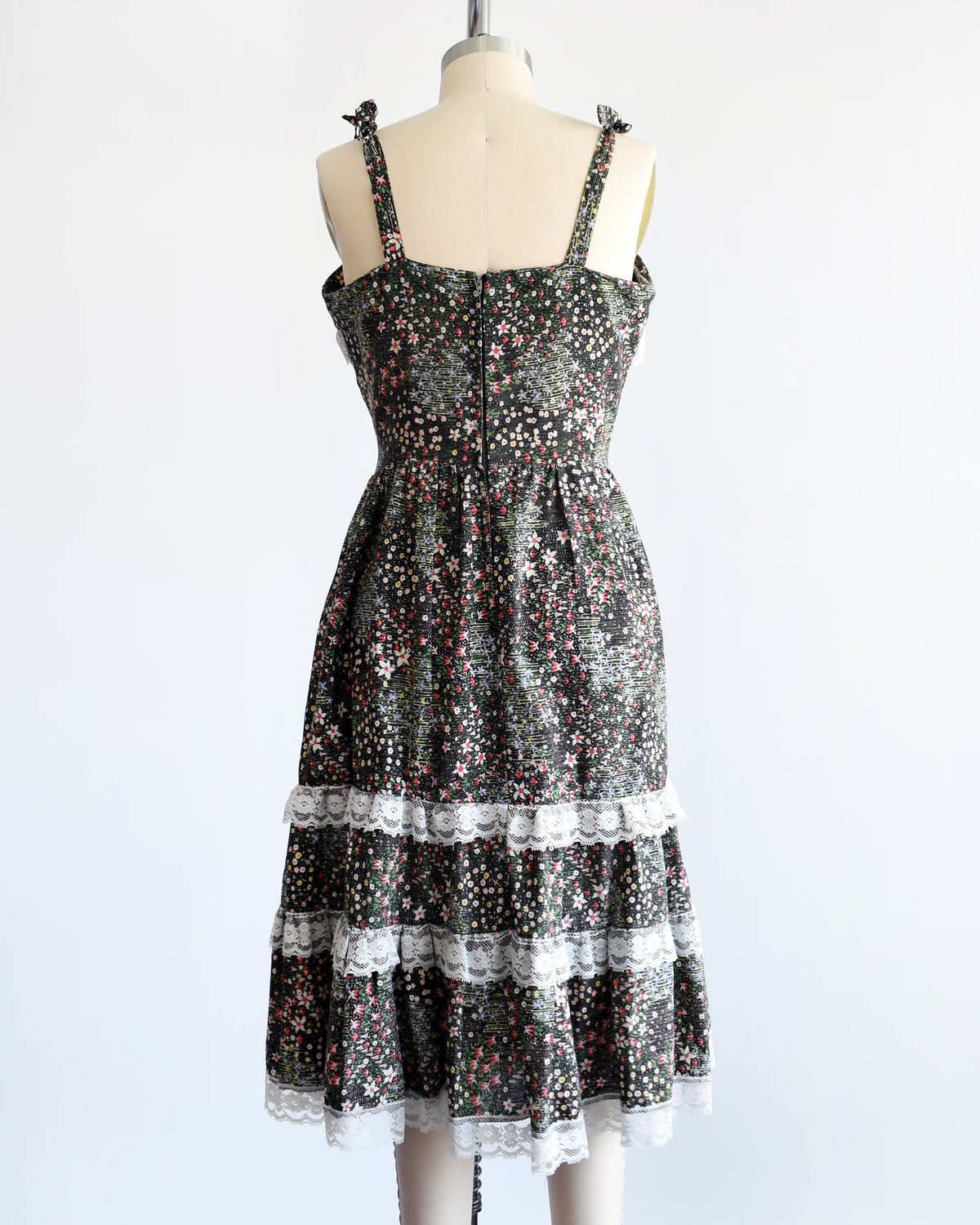 back view of a vintage 1970s dark floral and lace trim dress on a cream dress form against a white background