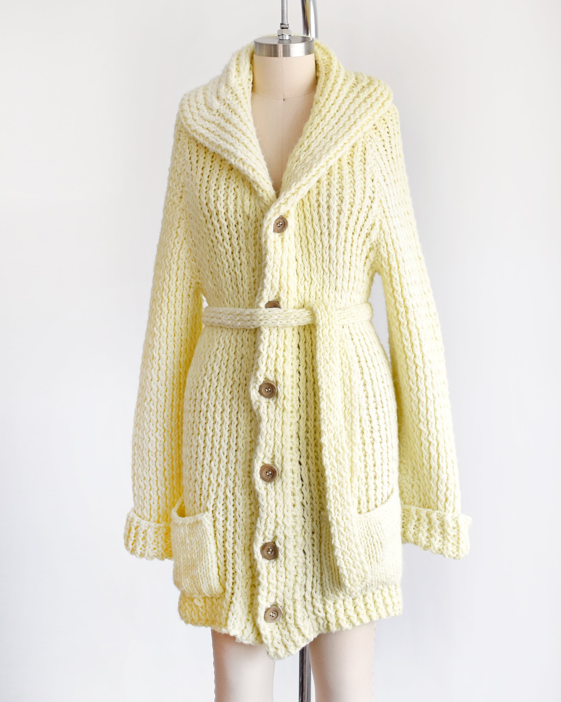 side front view of a vintage 1970s cream chunky knit cardigan with wood buttons down the front with a matching tie belt on a dress form.