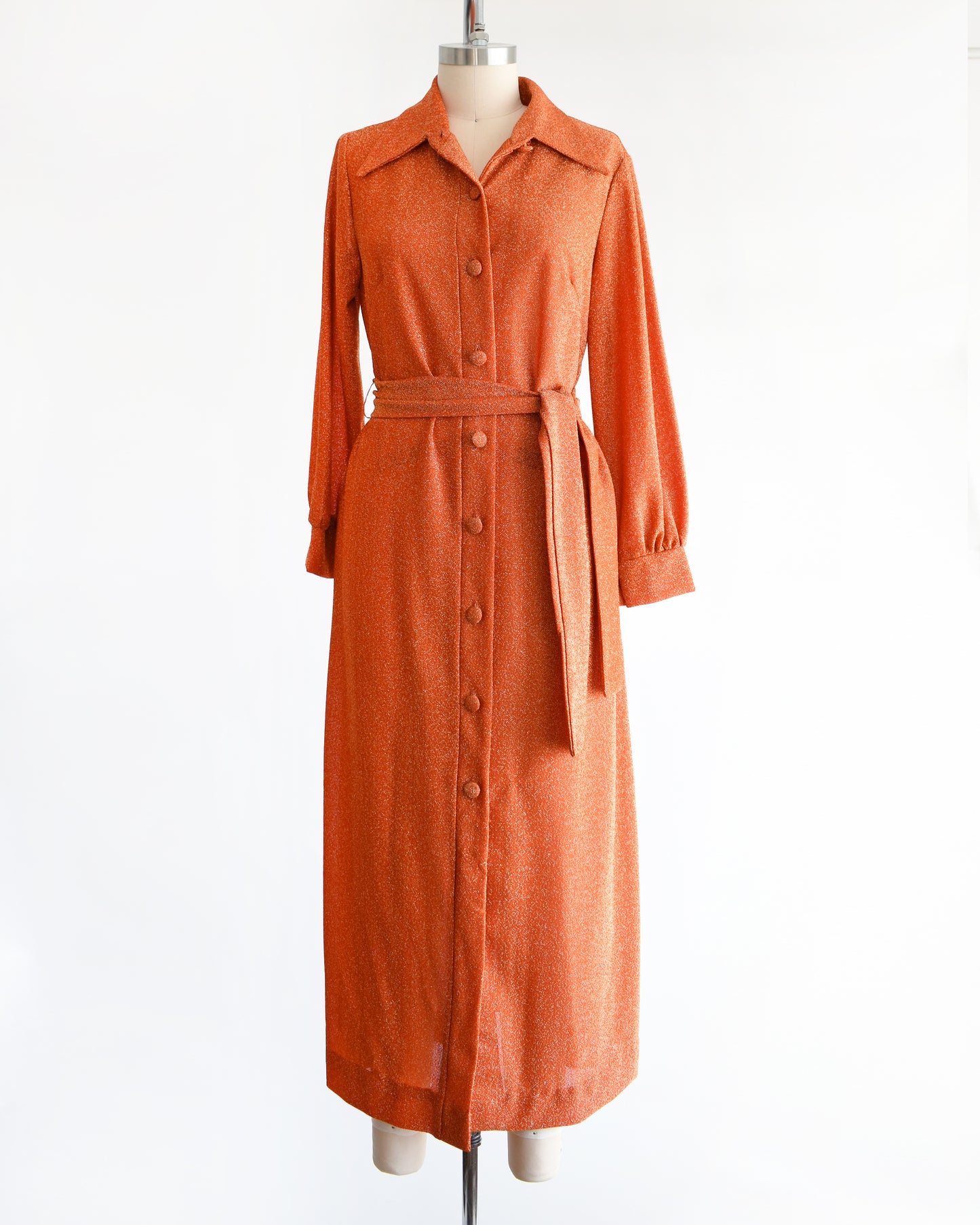 A vintage 1970s orange metallic dress on a mannequin against a white background