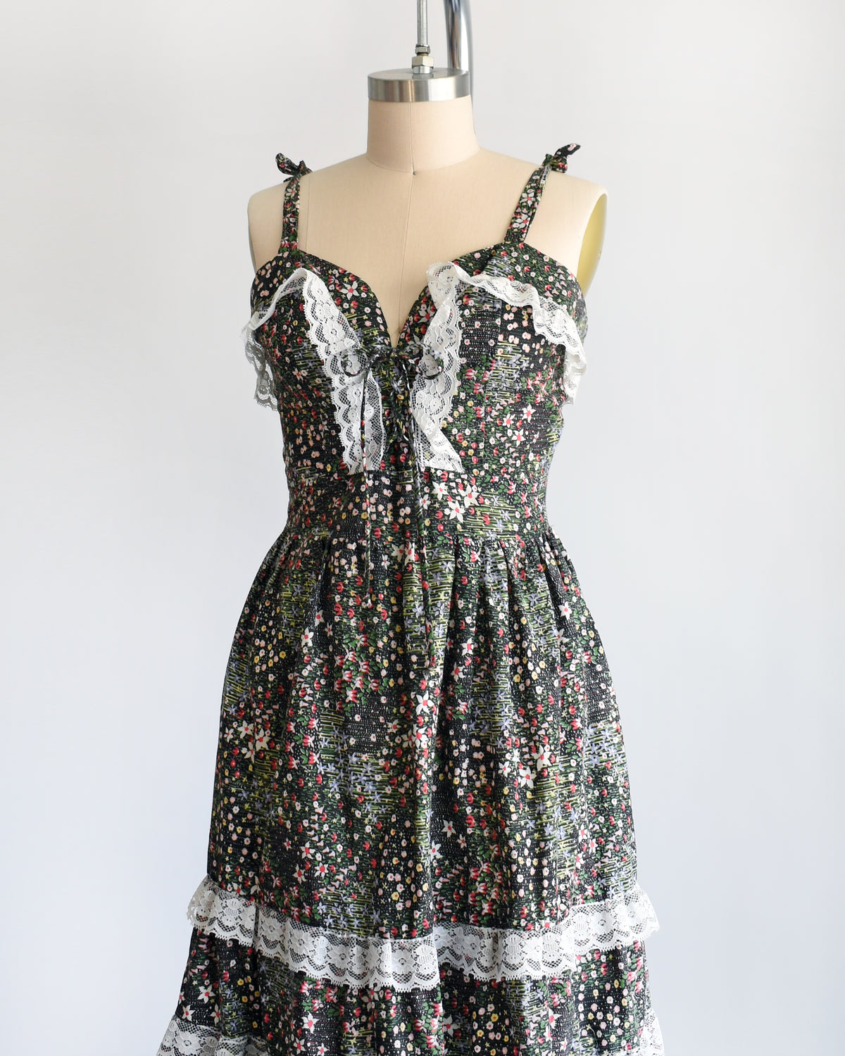 side front view of a vintage 1970s dark floral and lace trim dress on a cream dress form against a white background