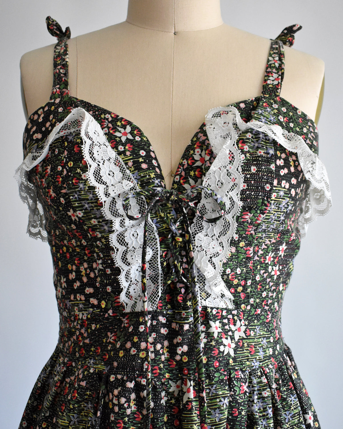 close up of a vintage 1970s dark floral and lace trim dress on a cream dress form against a white background
