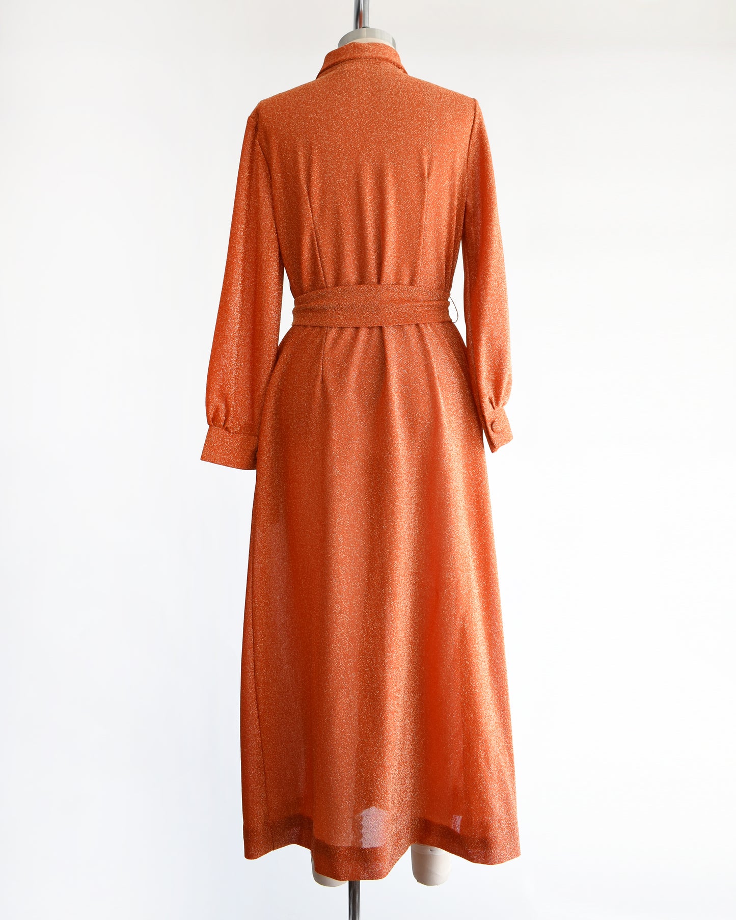 back view of a vintage 1970s orange metallic dress on a mannequin against a white background