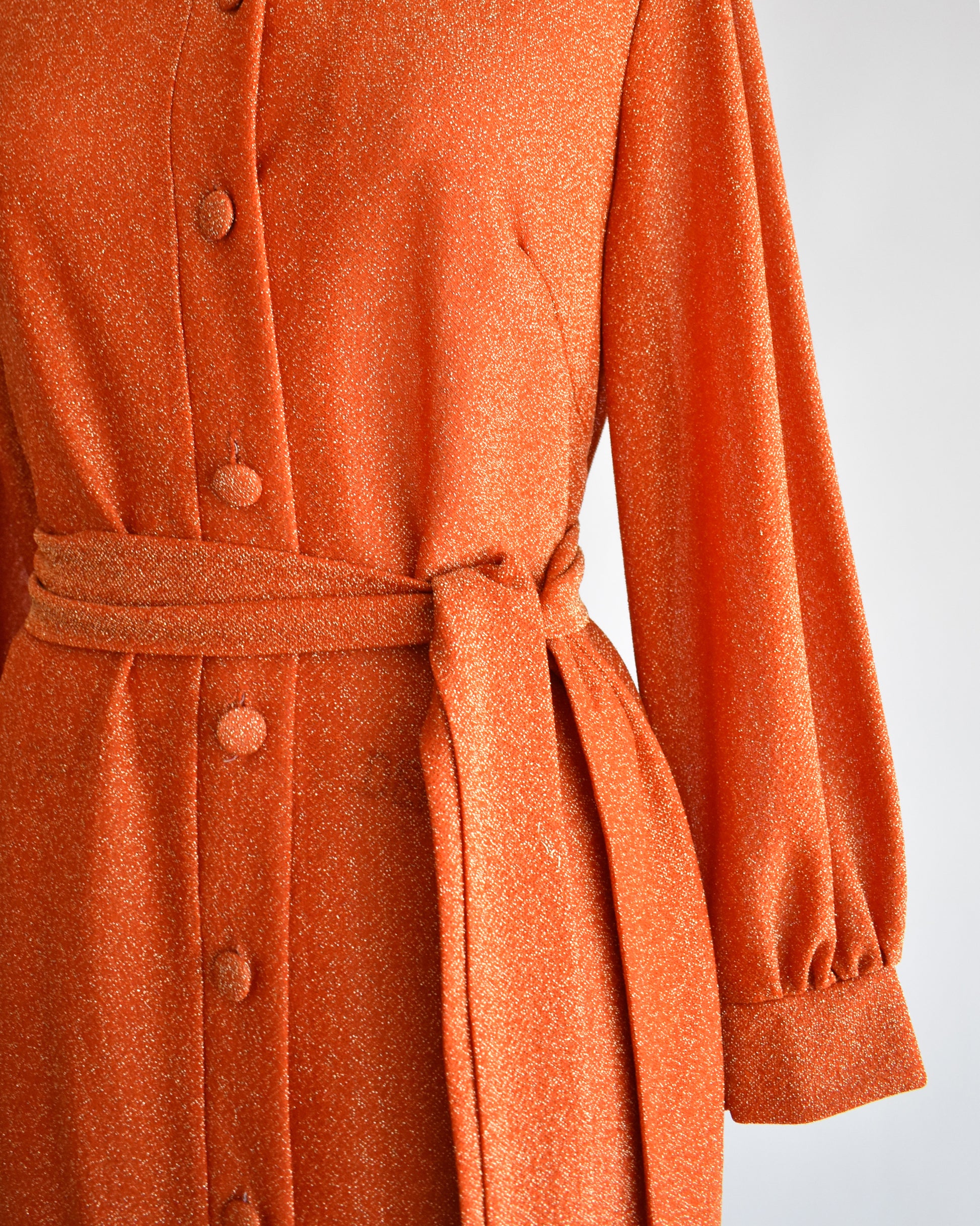 close up of the waist of a vintage 1970s orange metallic dress on a mannequin against a white background