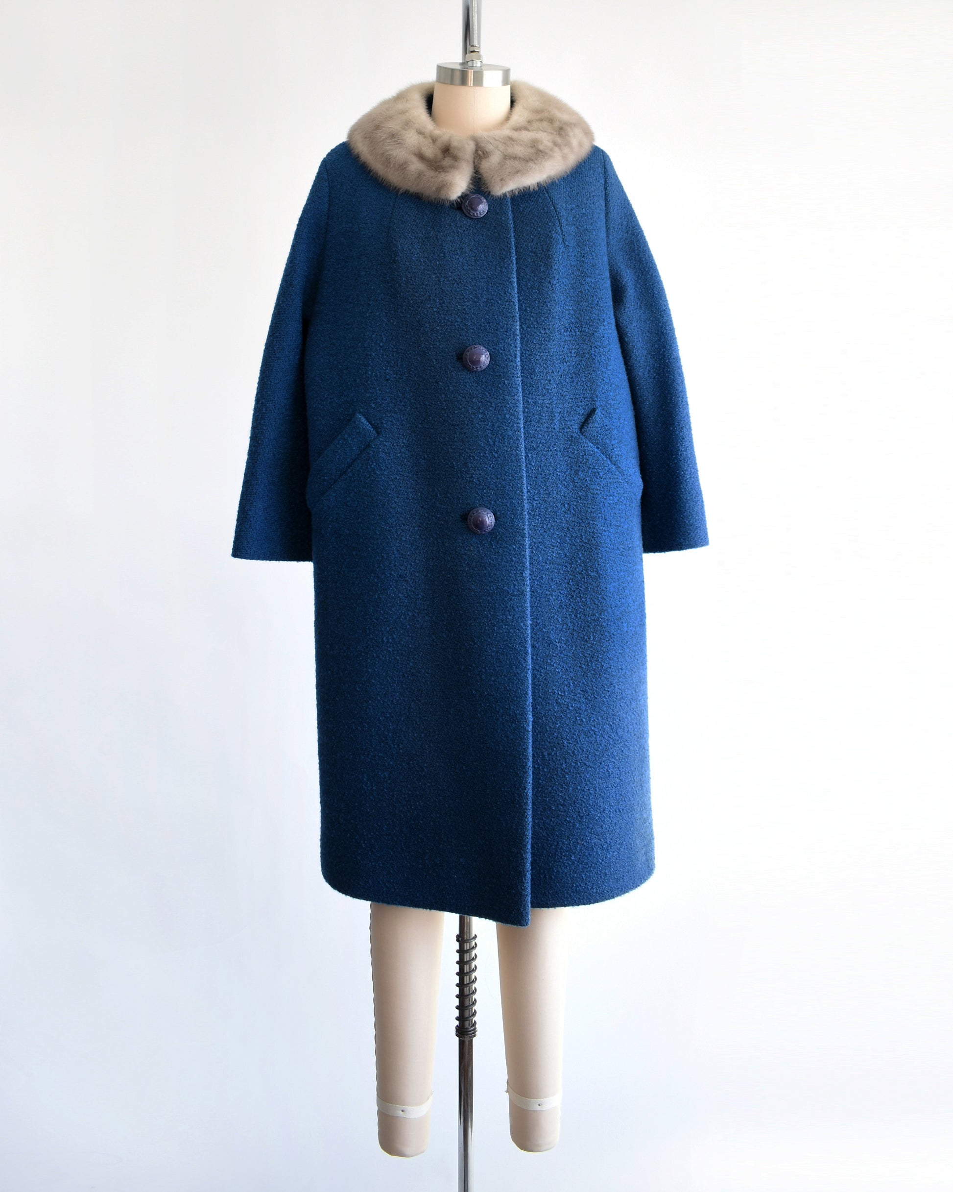 a vintage 1960s blue wool coat with gray fur trimmed collar on a mannequin against a white background
