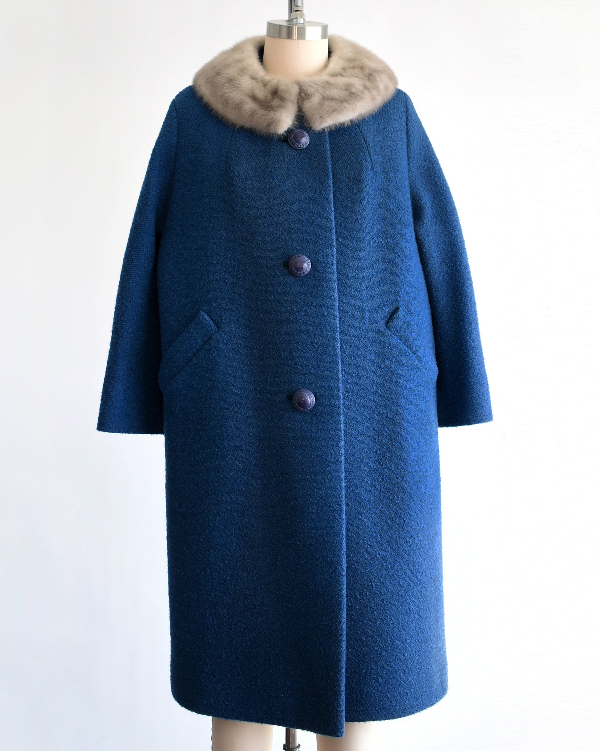 a vintage 1960s blue wool coat with gray fur trimmed collar on a mannequin against a white background
