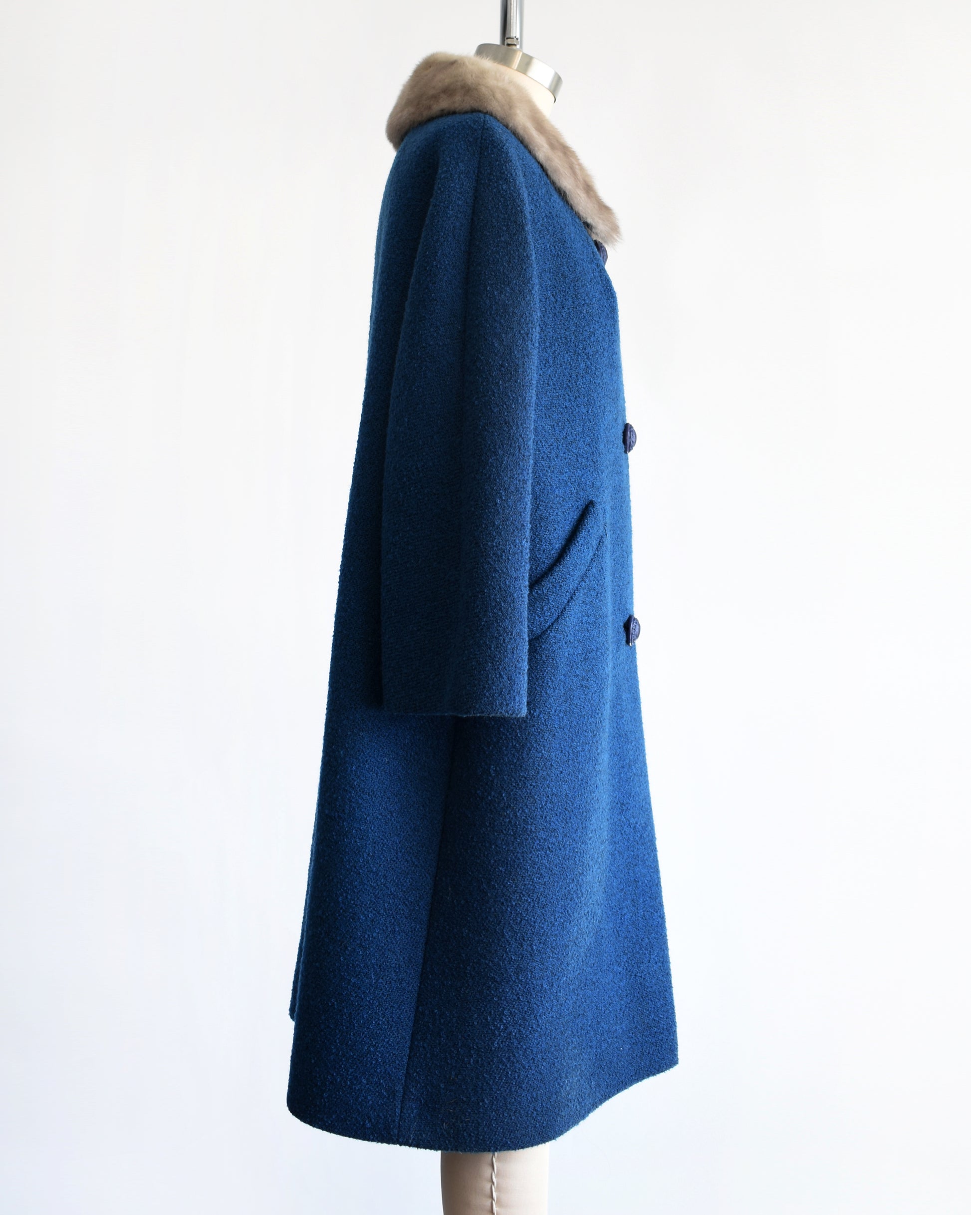 side view of a vintage 1960s blue wool coat with gray fur trimmed collar on a mannequin against a white background