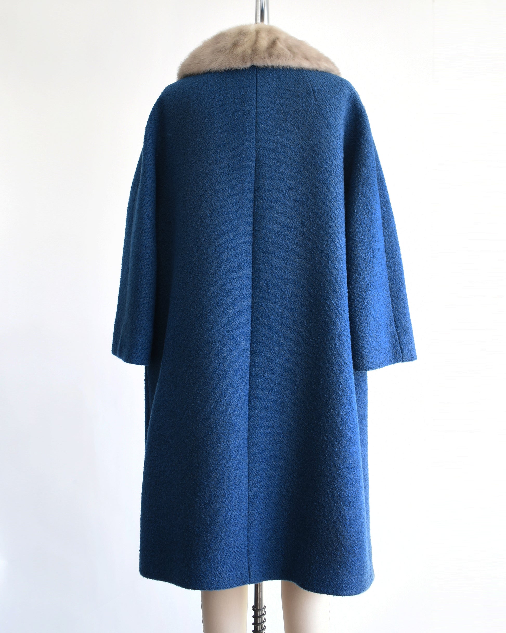 back view of a vintage 1960s blue wool coat with gray fur trimmed collar on a mannequin against a white background