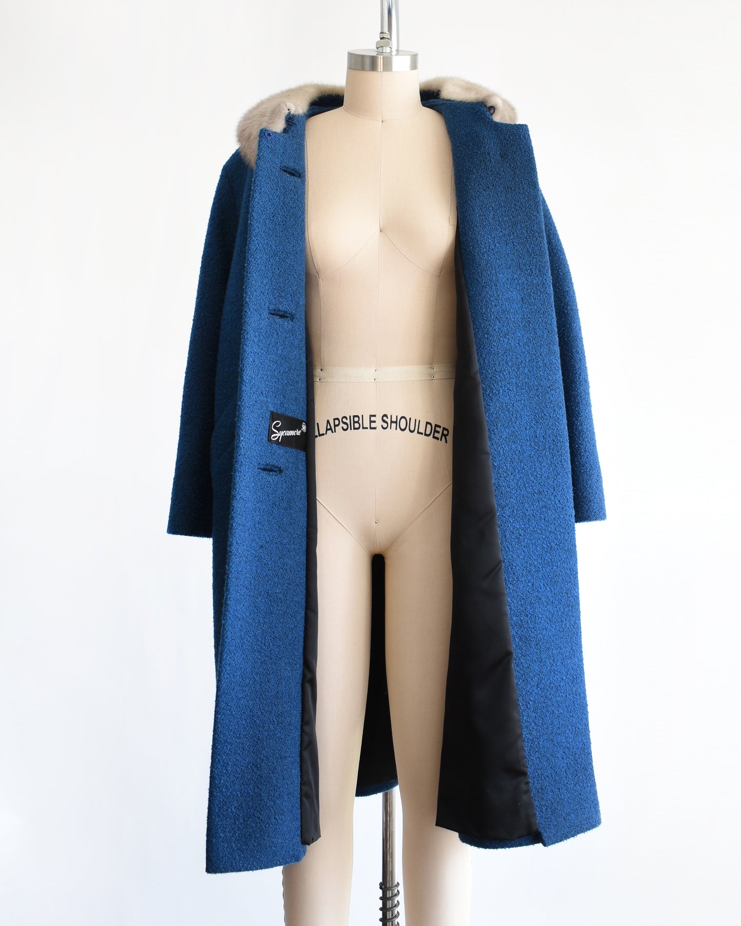 front view of a vintage 1960s blue wool coat with gray fur trimmed collar that's unbuttoned on a mannequin against a white background