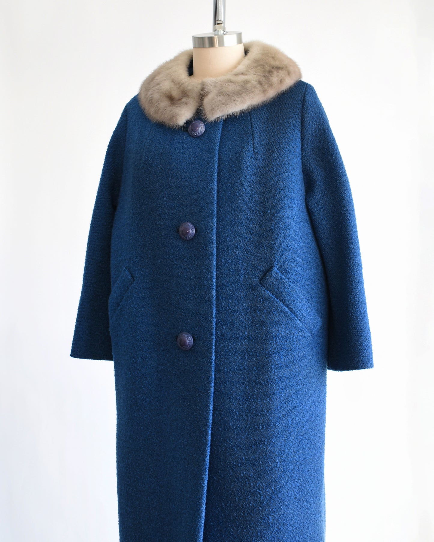 side front view of a vintage 1960s blue wool coat with gray fur trimmed collar on a mannequin against a white background