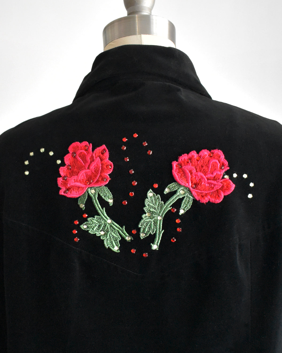 Black velvet shirt with red rose and green leaf embroidery on the back, displayed on a mannequin against a white background.