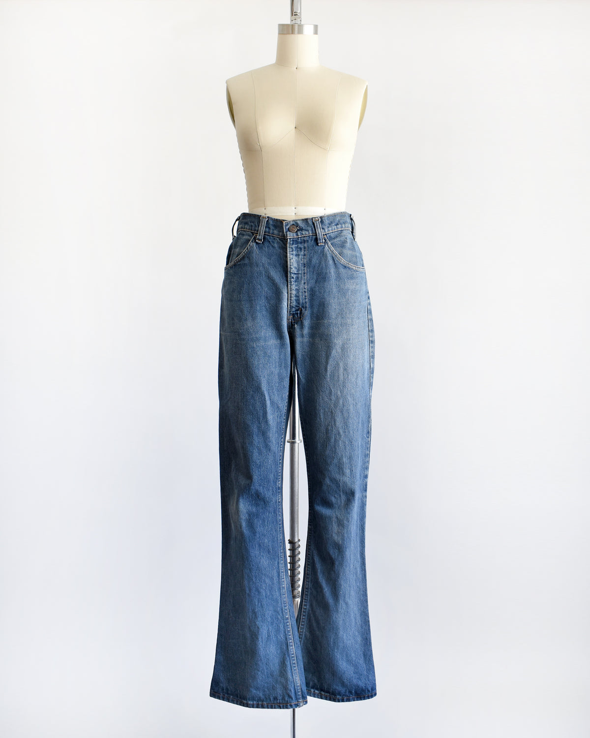 A pair of medium-wash blue denim flare vintage Levi's jeans displayed on a cream-colored dress form mannequin against a plain white background.