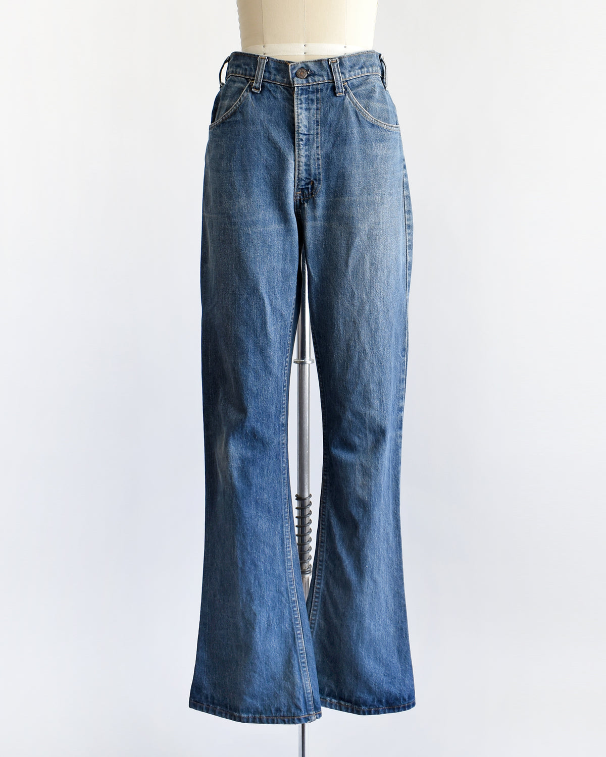 A pair of medium-wash blue denim flare vintage Levi's jeans displayed on a cream-colored dress form mannequin against a plain white background.