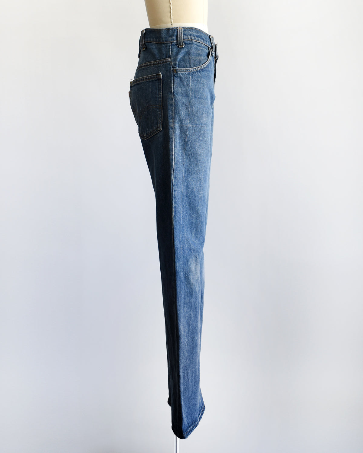 side view of a pair of medium-wash blue denim flare vintage Levi's jeans displayed on a cream-colored dress form mannequin against a plain white background.