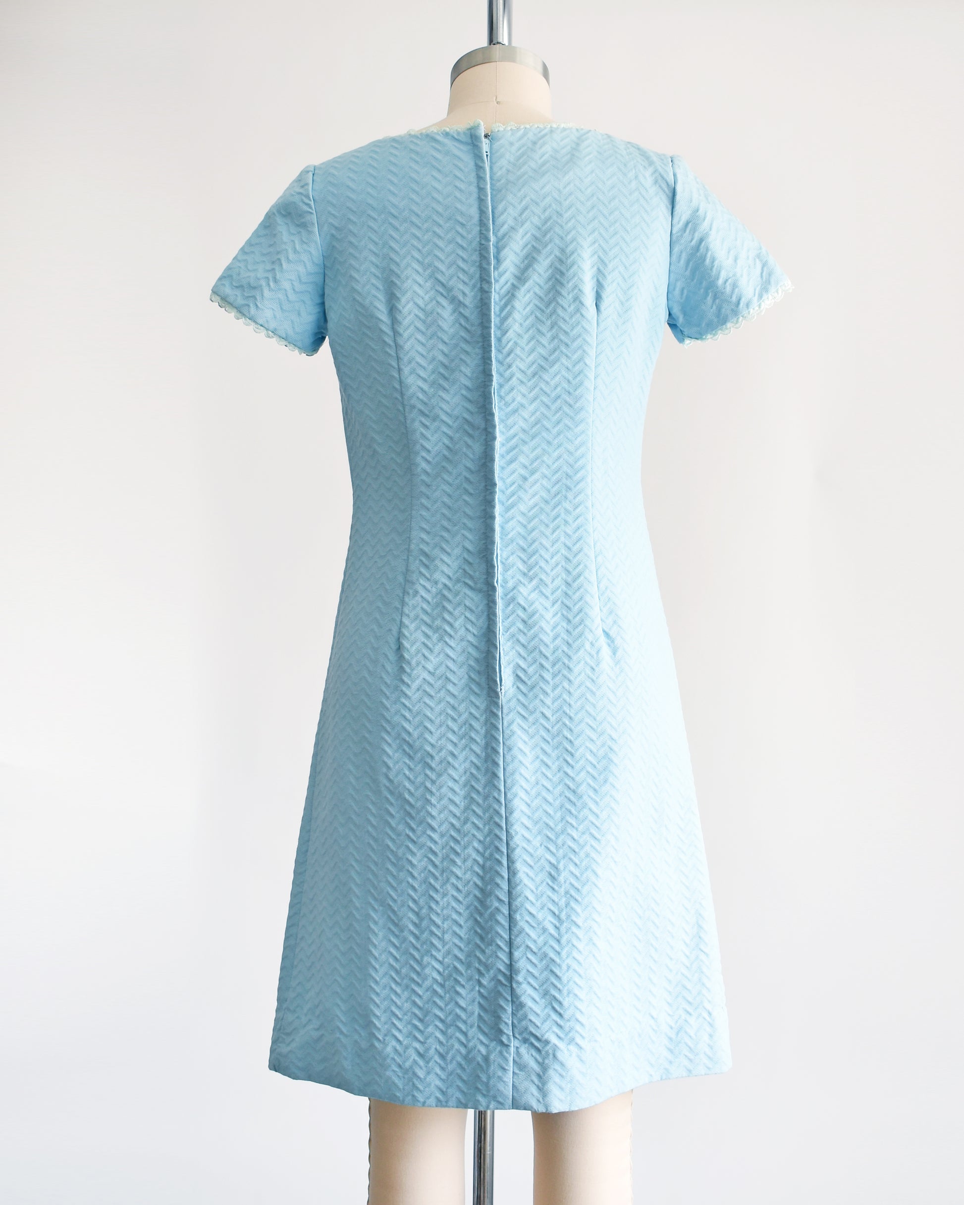 Back view of a A vintage 1960s mod dress that has textured light blue chevron striped knit with alternating ribbing and lace trim.