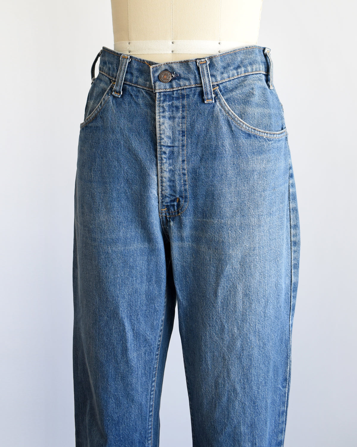 side front view of a pair of medium-wash blue denim flare vintage Levi's jeans displayed on a cream-colored dress form mannequin against a plain white background.