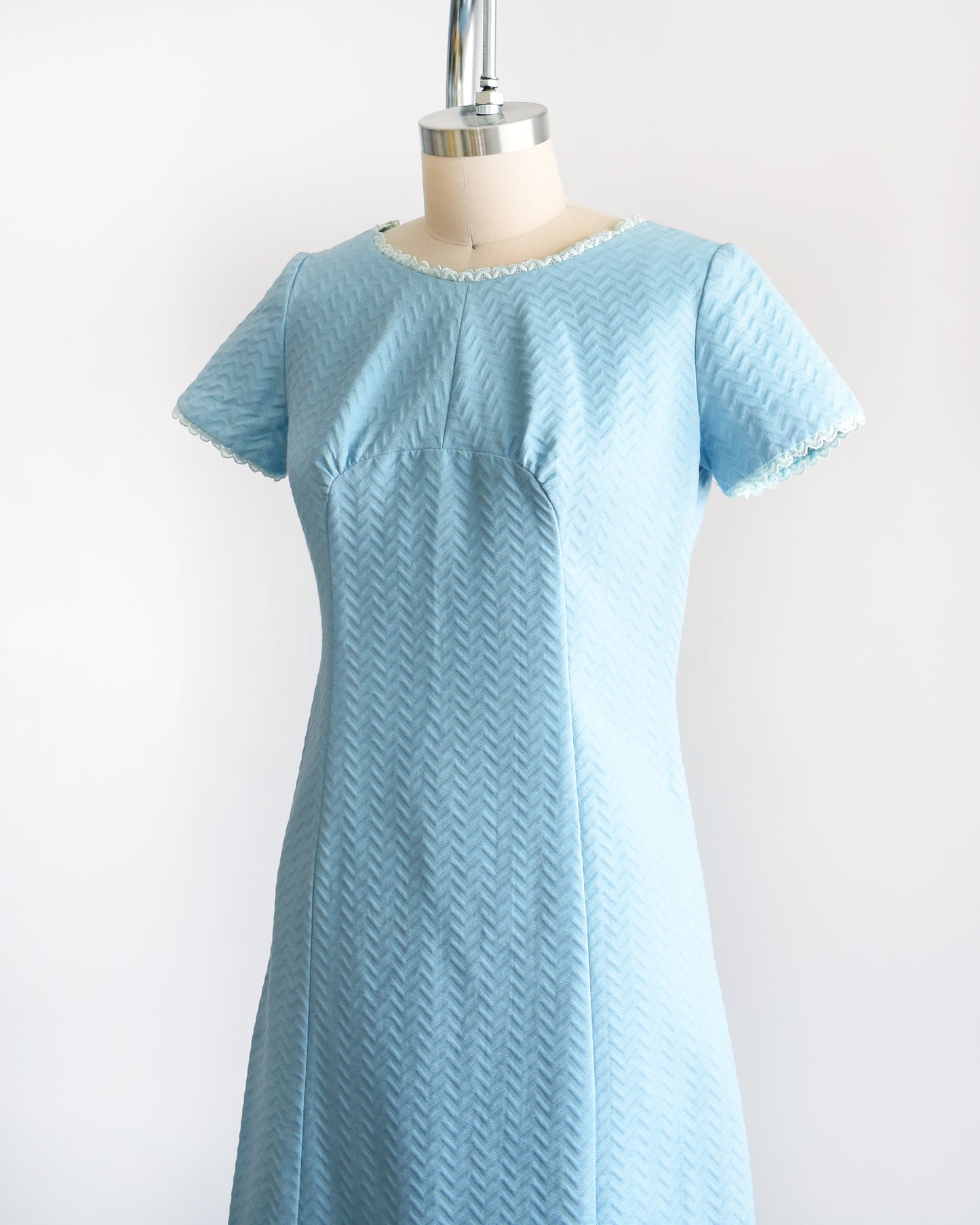 Side front view of a A vintage 1960s mod dress that has textured light blue chevron striped knit with alternating ribbing and lace trim.