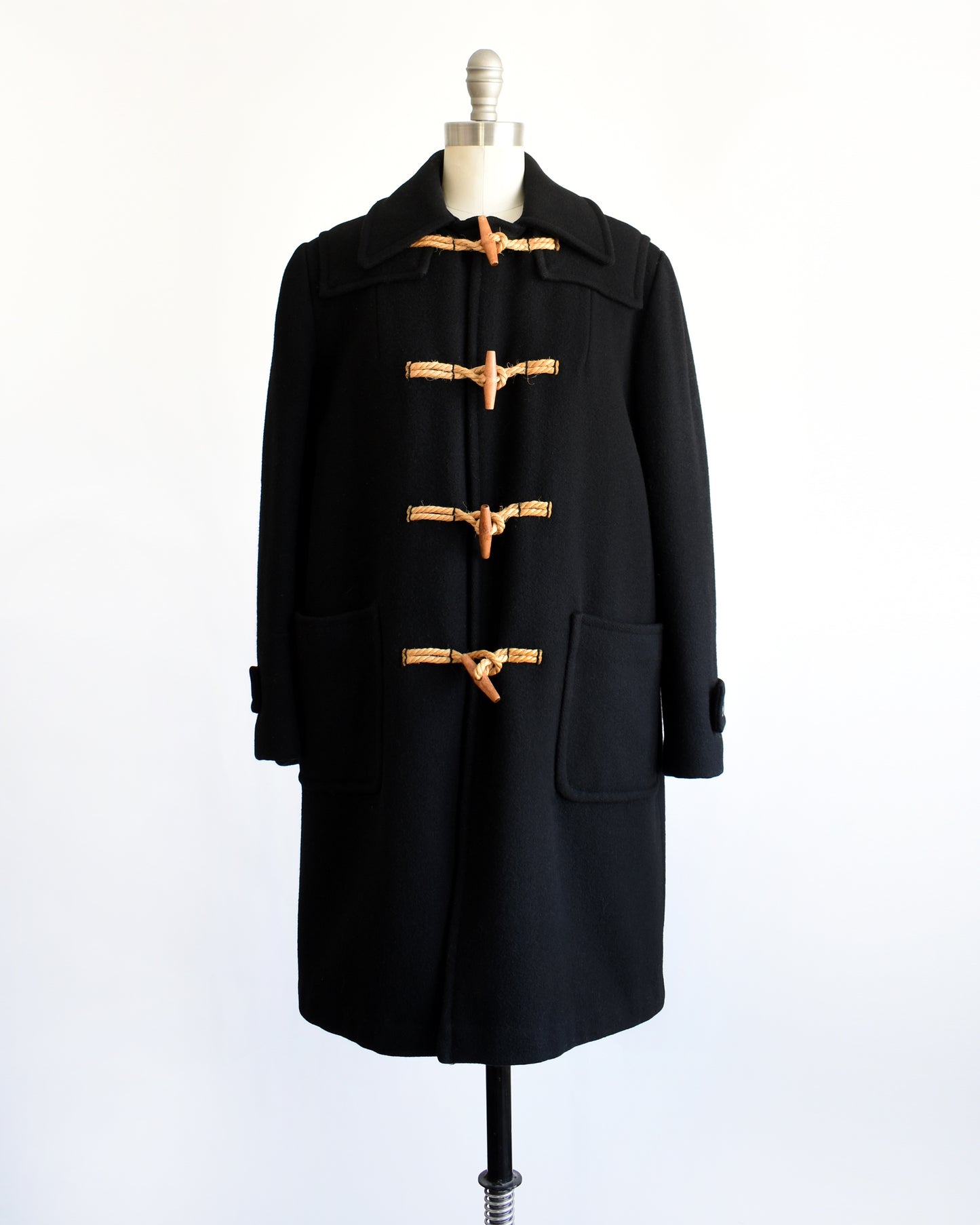 a vintage 1960s black coat with toggle buttons on a mannequin against a white background