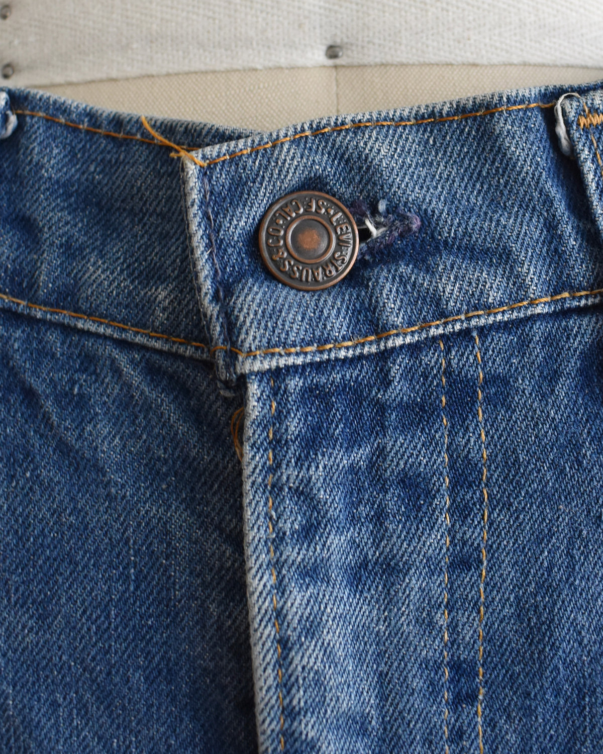 close up of the Levi's button on a pair of medium-wash blue denim flare vintage Levi's jeans displayed on a cream-colored dress form mannequin