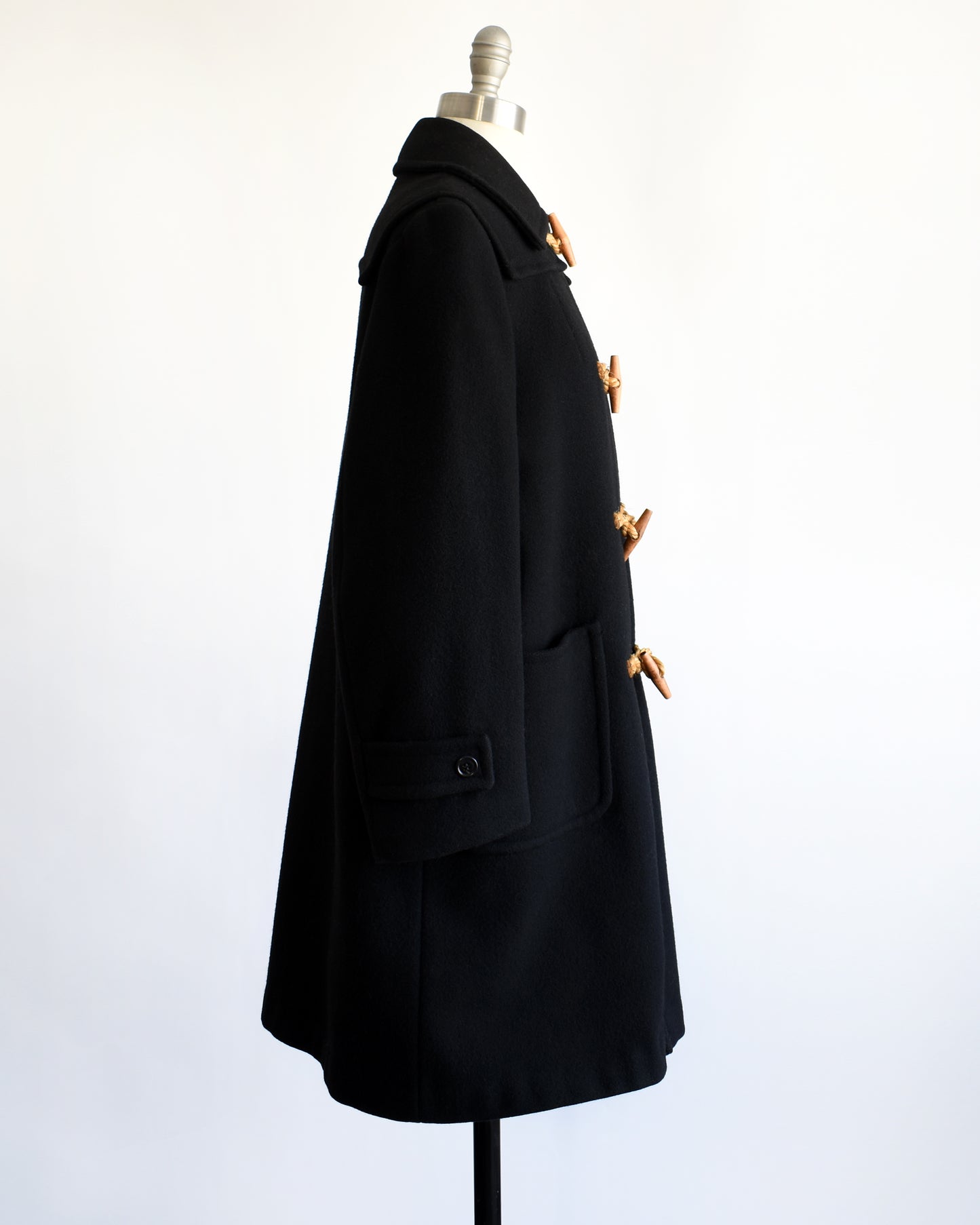 side view of a vintage 1960s black coat with toggle buttons on a mannequin against a white background