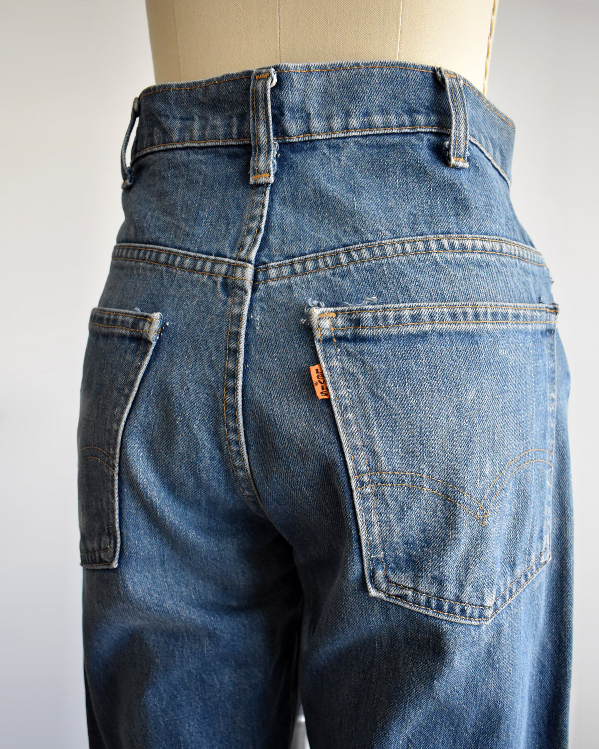 Rear view of vintage blue denim jeans on a mannequin, showing the back pockets, belt loops, and a small orange Levi's tab.