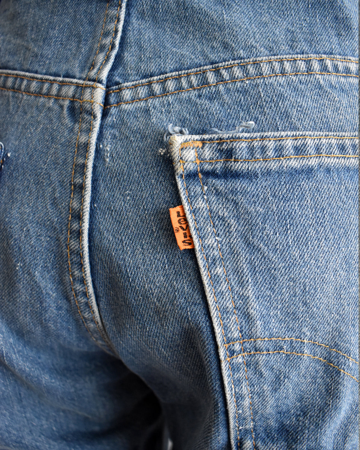Close-up of the back pocket of blue denim jeans with a visible orange Levi's brand tab.