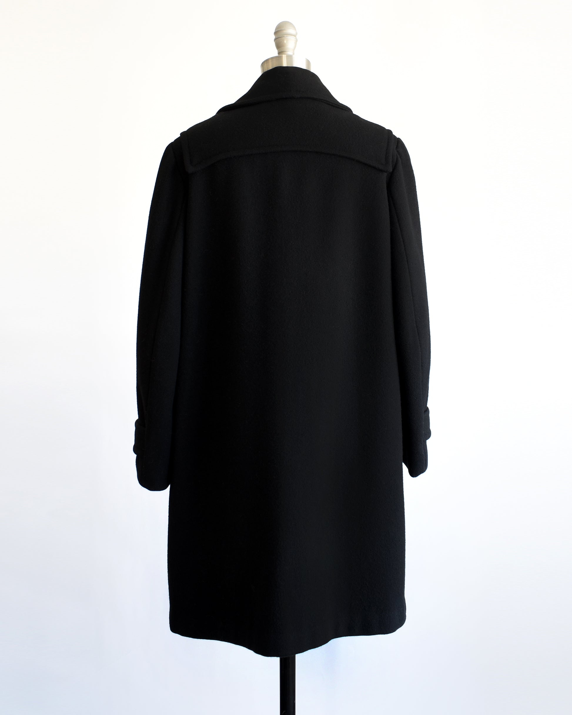 back view of a vintage 1960s black coat with toggle buttons on a mannequin against a white background