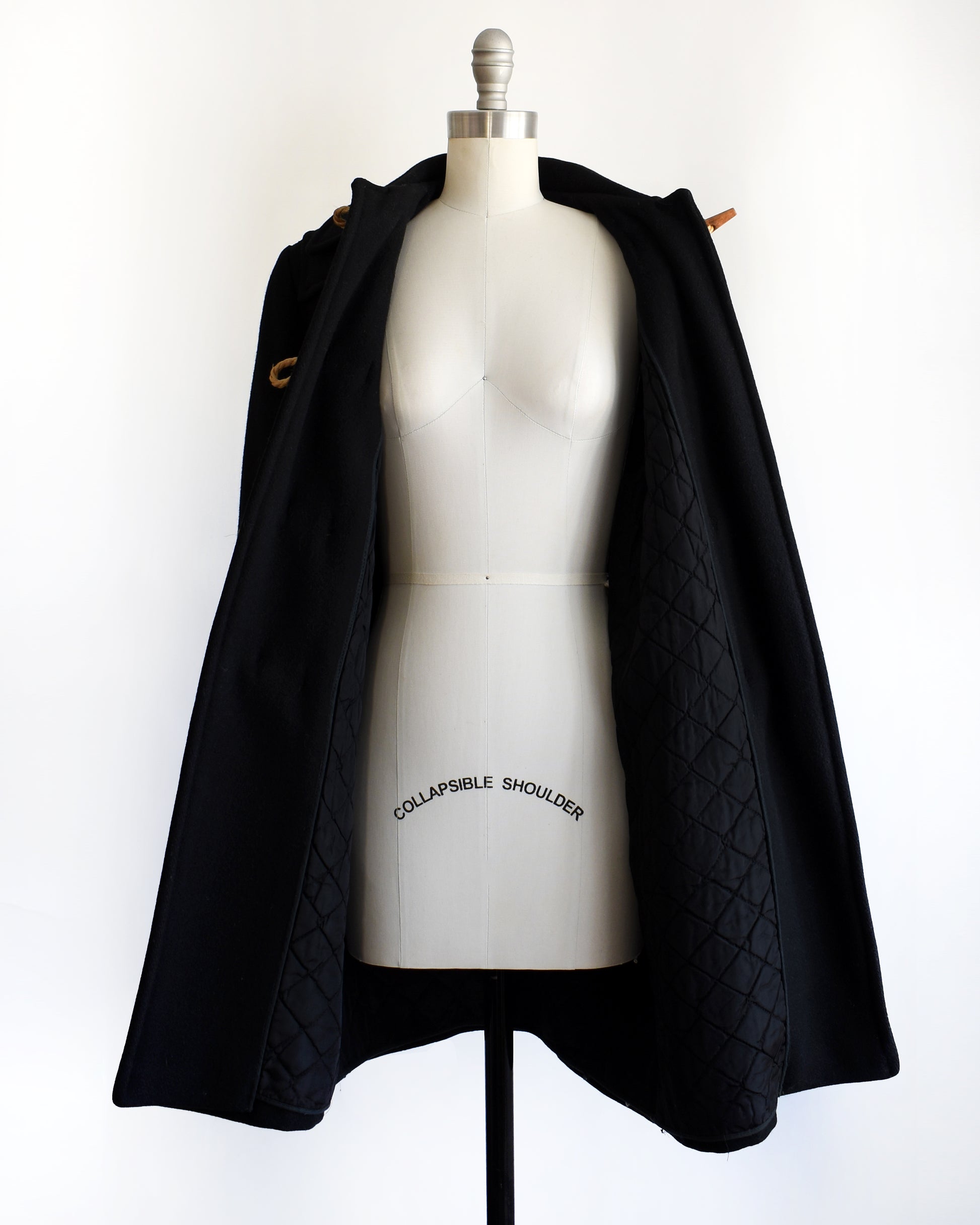 a vintage 1960s black coat with toggle buttons open showing the quilted lining on a mannequin against a white background