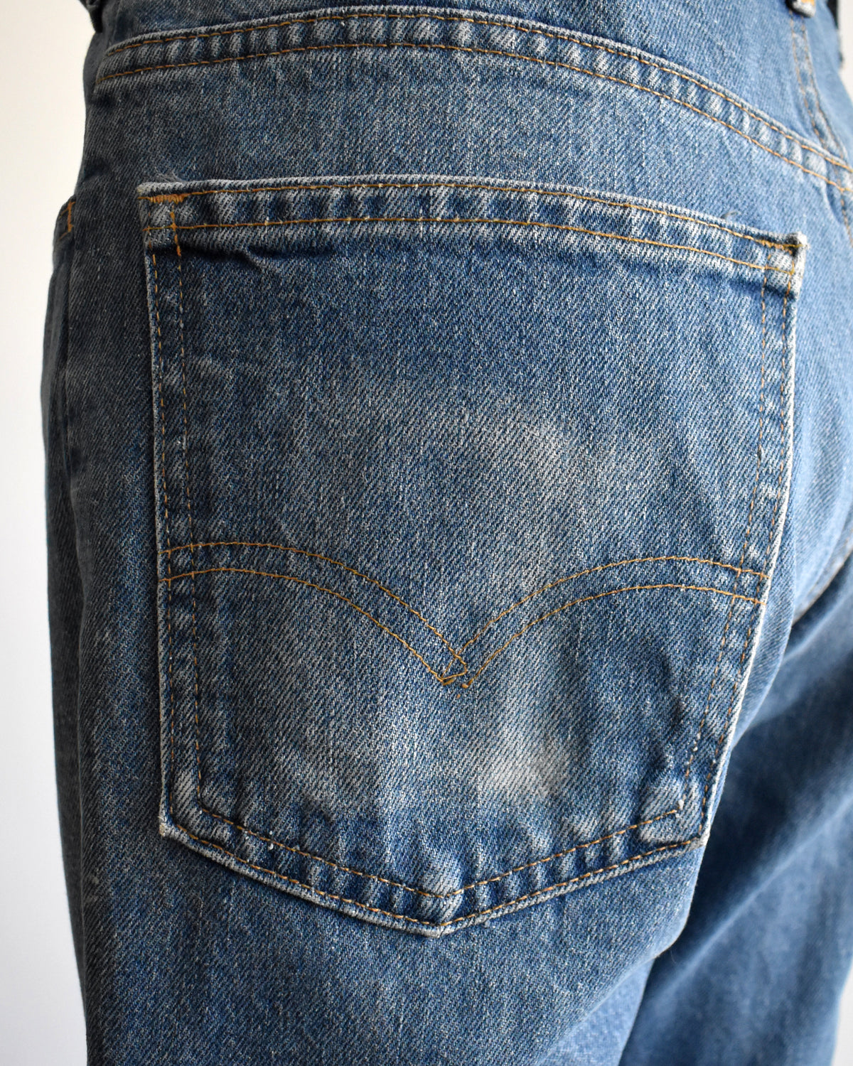 Close-up of the back pocket of blue denim jeans, showing the classic curved stitching and fabric texture.