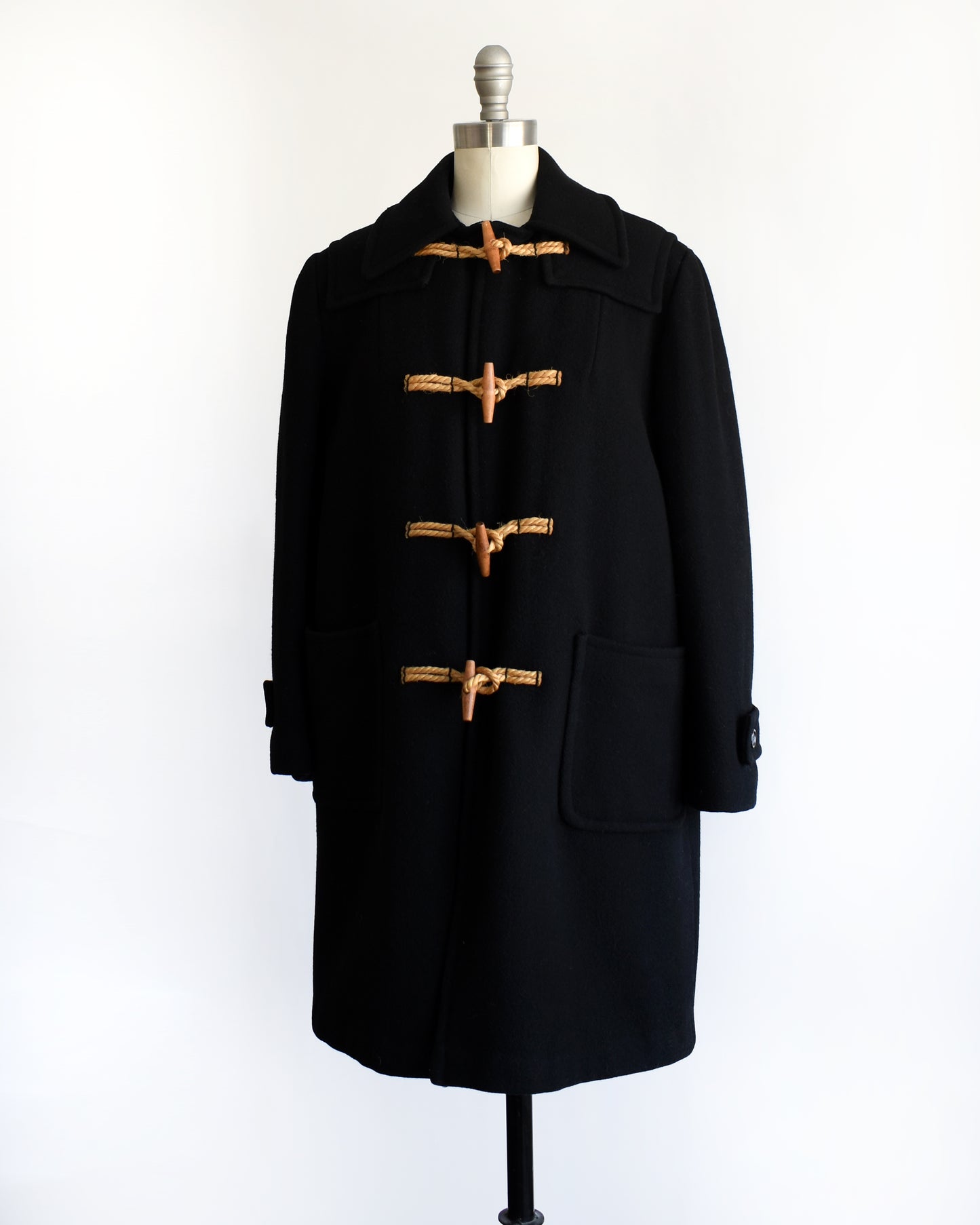 side view of a vintage 1960s black coat with toggle buttons on a mannequin against a white background