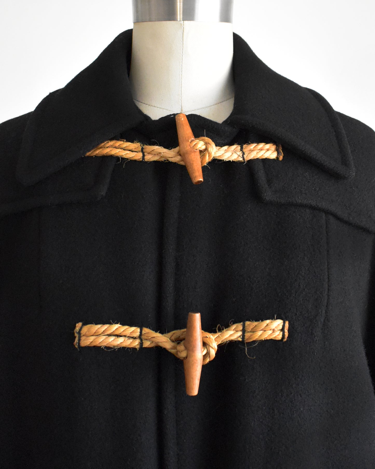 close up of a vintage 1960s black coat with toggle buttons on a mannequin against a white background